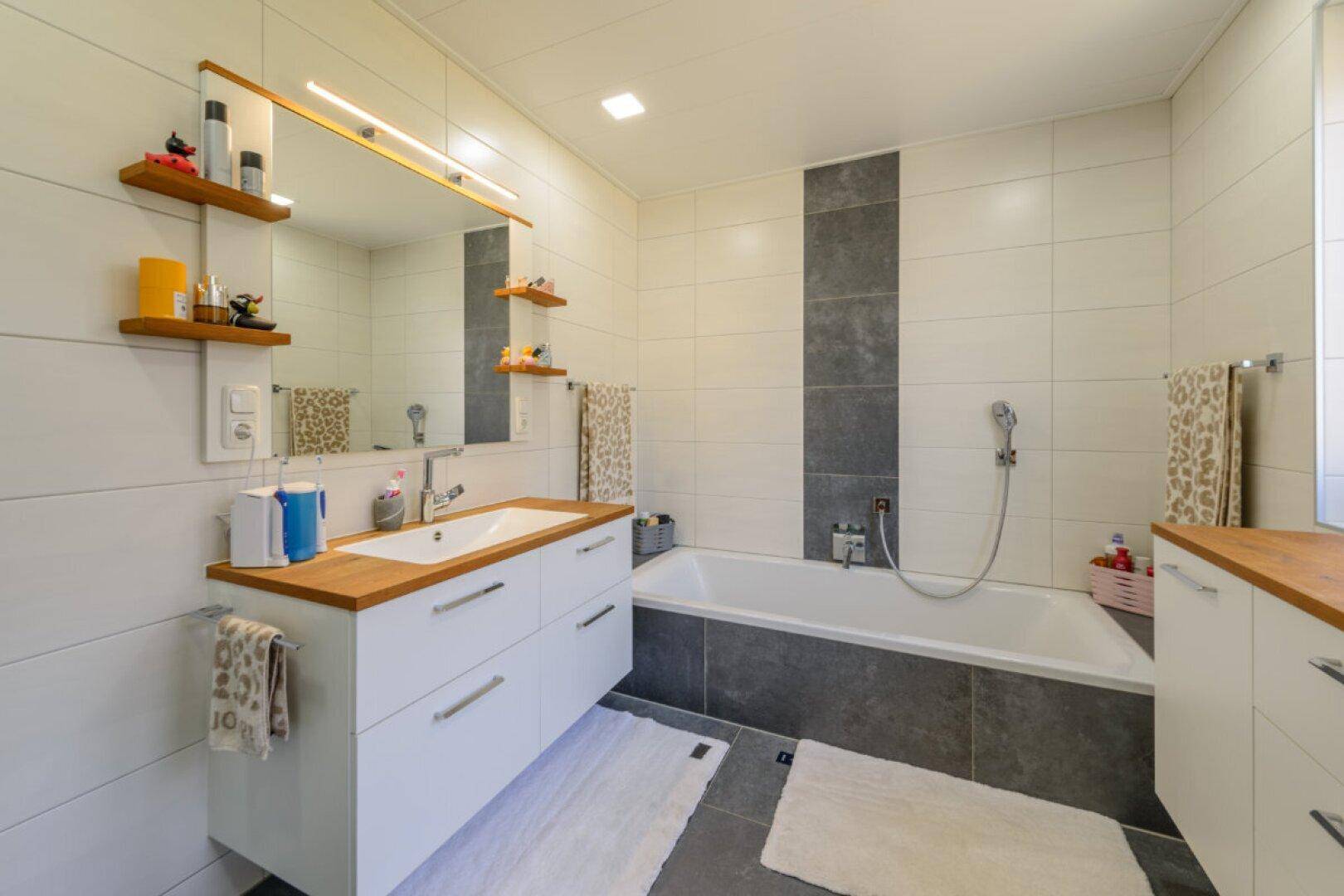 Modernes Badezimmer mit Waschtisch, Badewanne und Fliesen in Weiß und Grau.