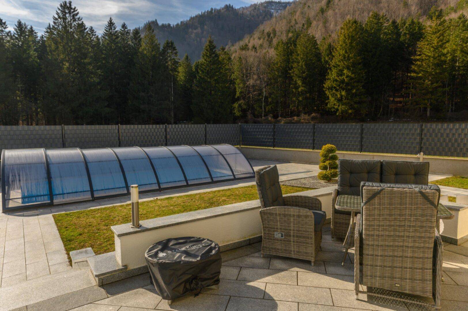 Gemütliche Terrasse mit Gartenmöbeln, Blick auf den Pool und die umliegende Natur.