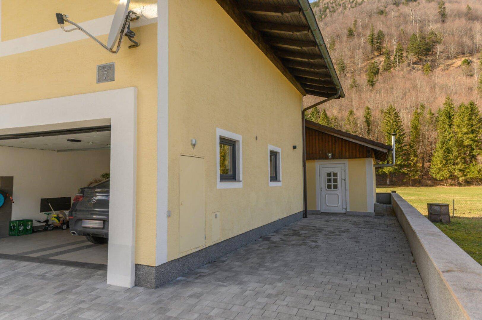 Seitenansicht des Hauses mit Garageneinfahrt und Blick auf die umliegende Berglandschaft.