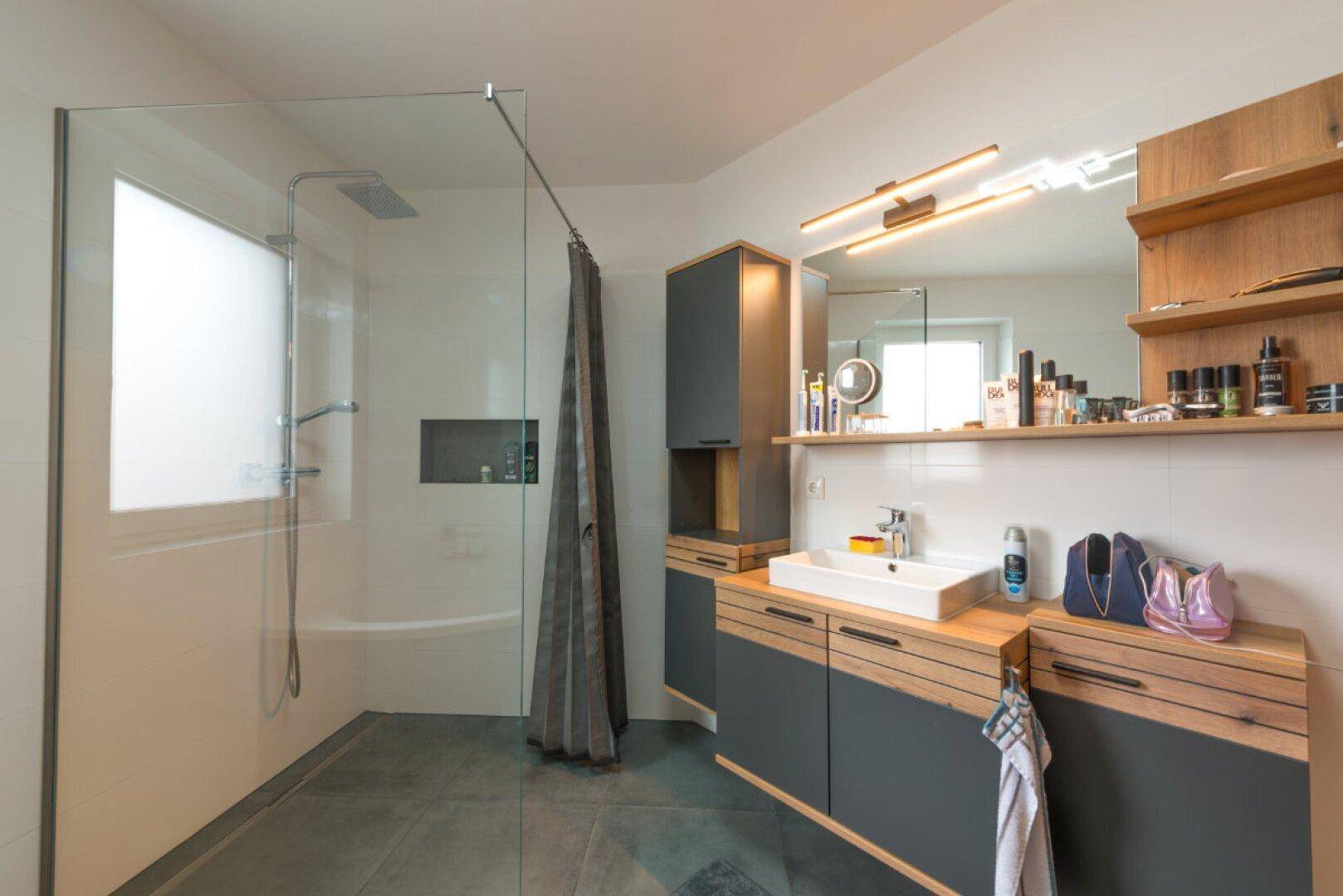Geräumiges Badezimmer mit großem Waschtisch, Spiegel und begehbarer Dusche.