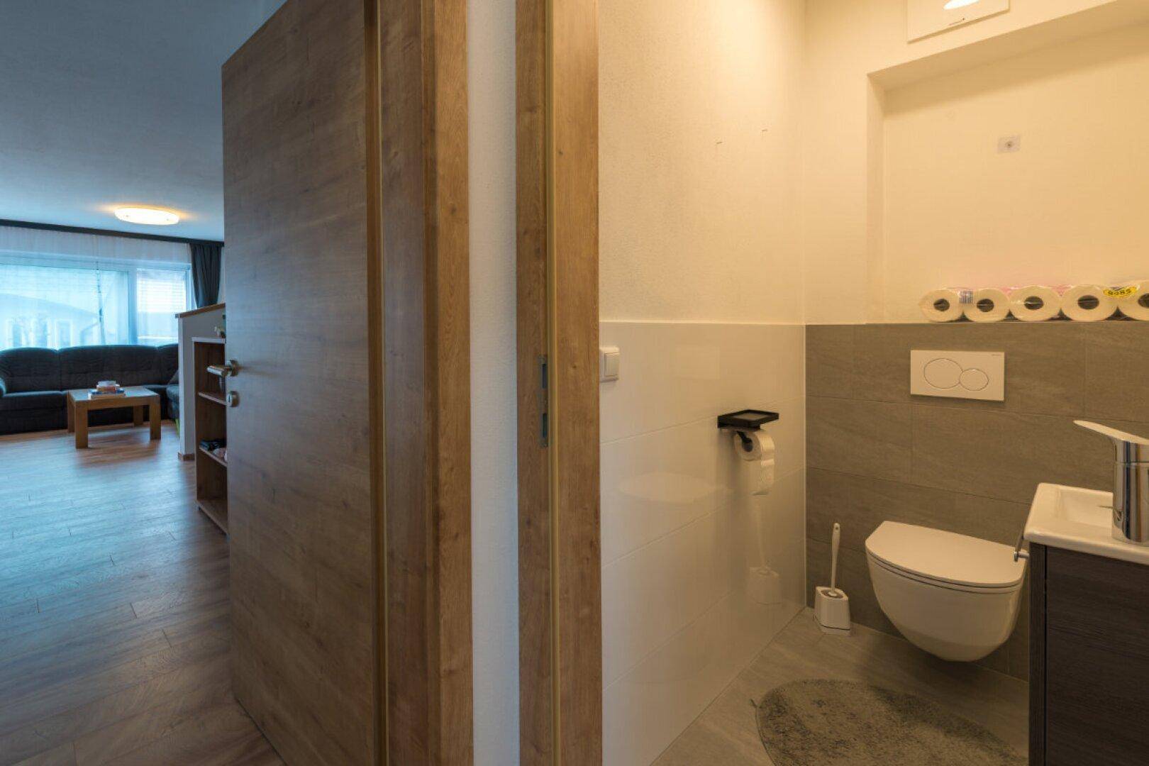 Modernes Gäste-WC mit Wand-WC, kleinem Waschbecken und grauen Fliesen.
