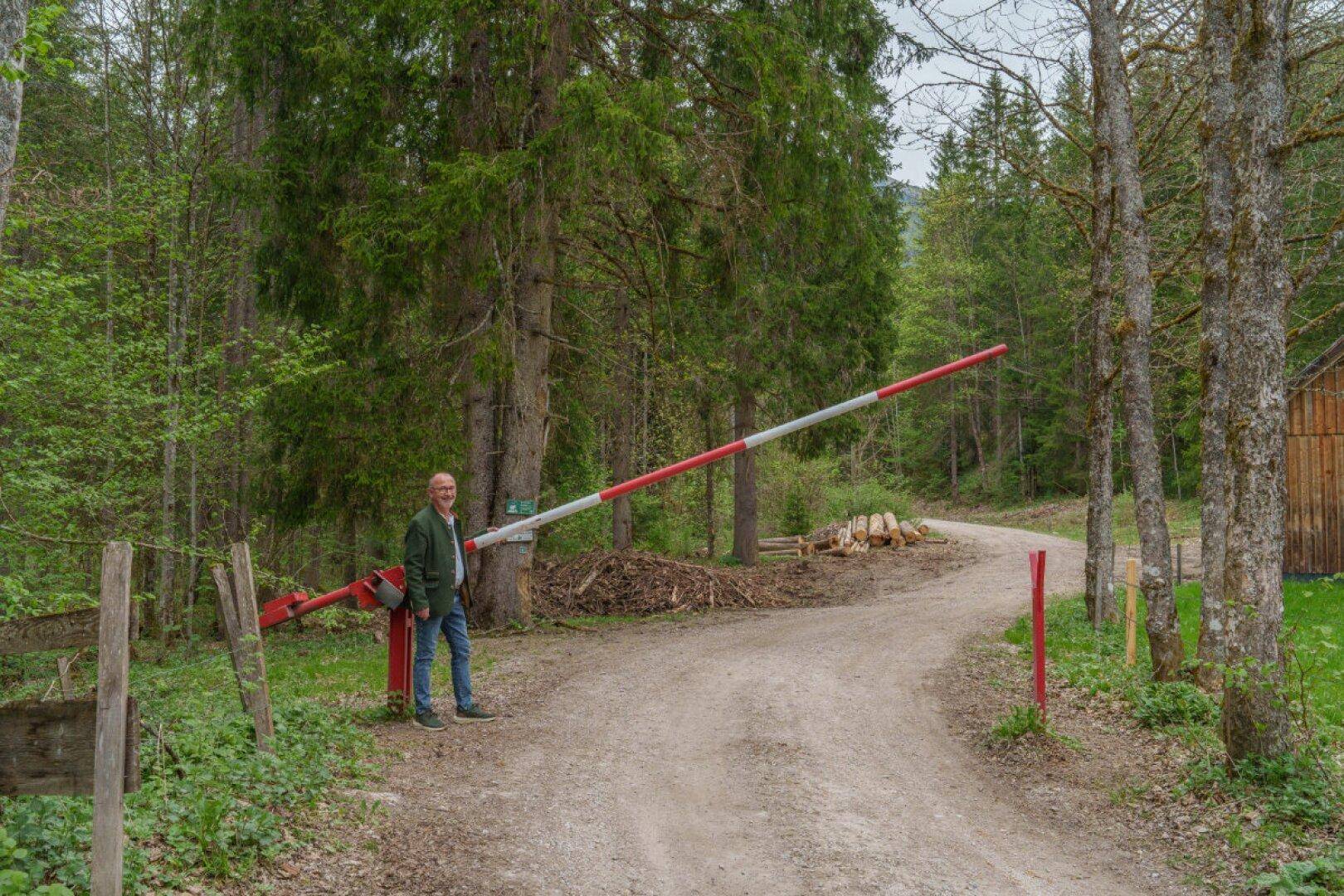 Ein Mann steht an einer Schranke auf einem Waldweg, der zu einer abgelegenen Hütte führt.