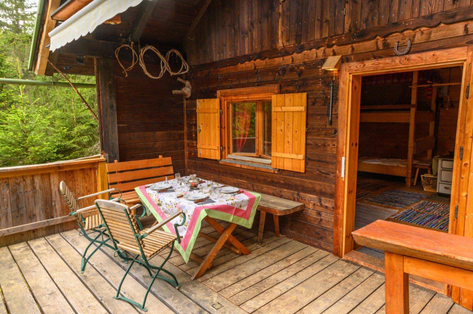 Rustikale Holzterrasse mit Esstisch und Stühlen, direkt an der Holzhütte gelegen.