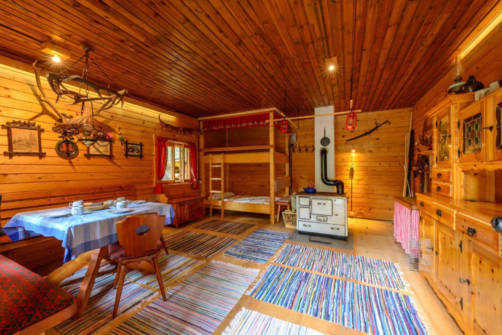 Rustikaler Wohn- und Essbereich mit Holzvertäfelung, Etagenbett und traditionellem Ofen.