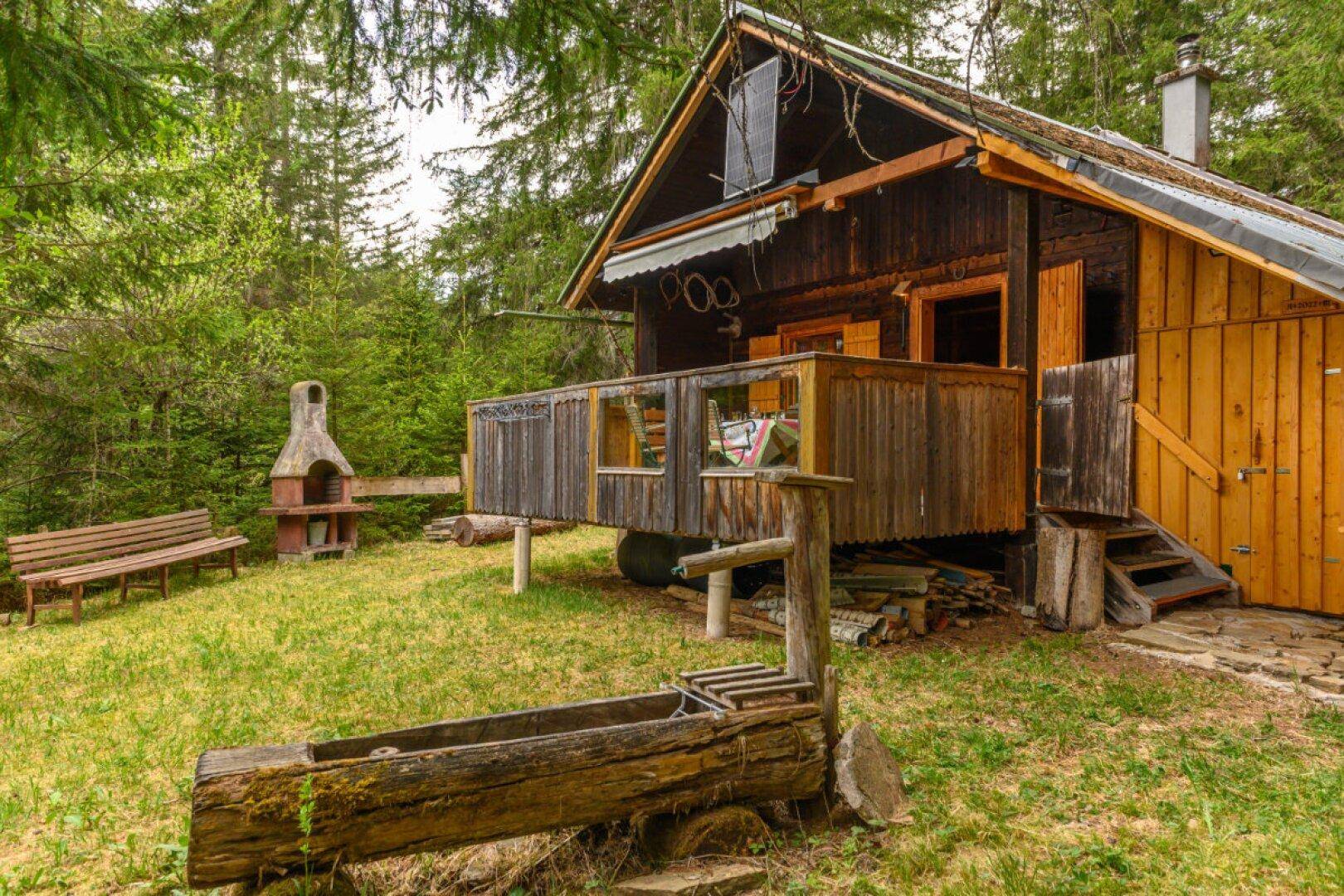 Gartenbereich vor der Holzhütte mit Grillplatz, Holzbank und rustikalem Wassertrog.