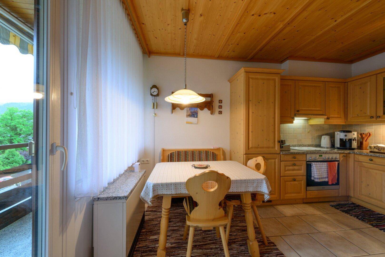 Traditionelle Wohnküche mit Holzeinbauten, Essbereich und Zugang zum Balkon mit Bergblick.