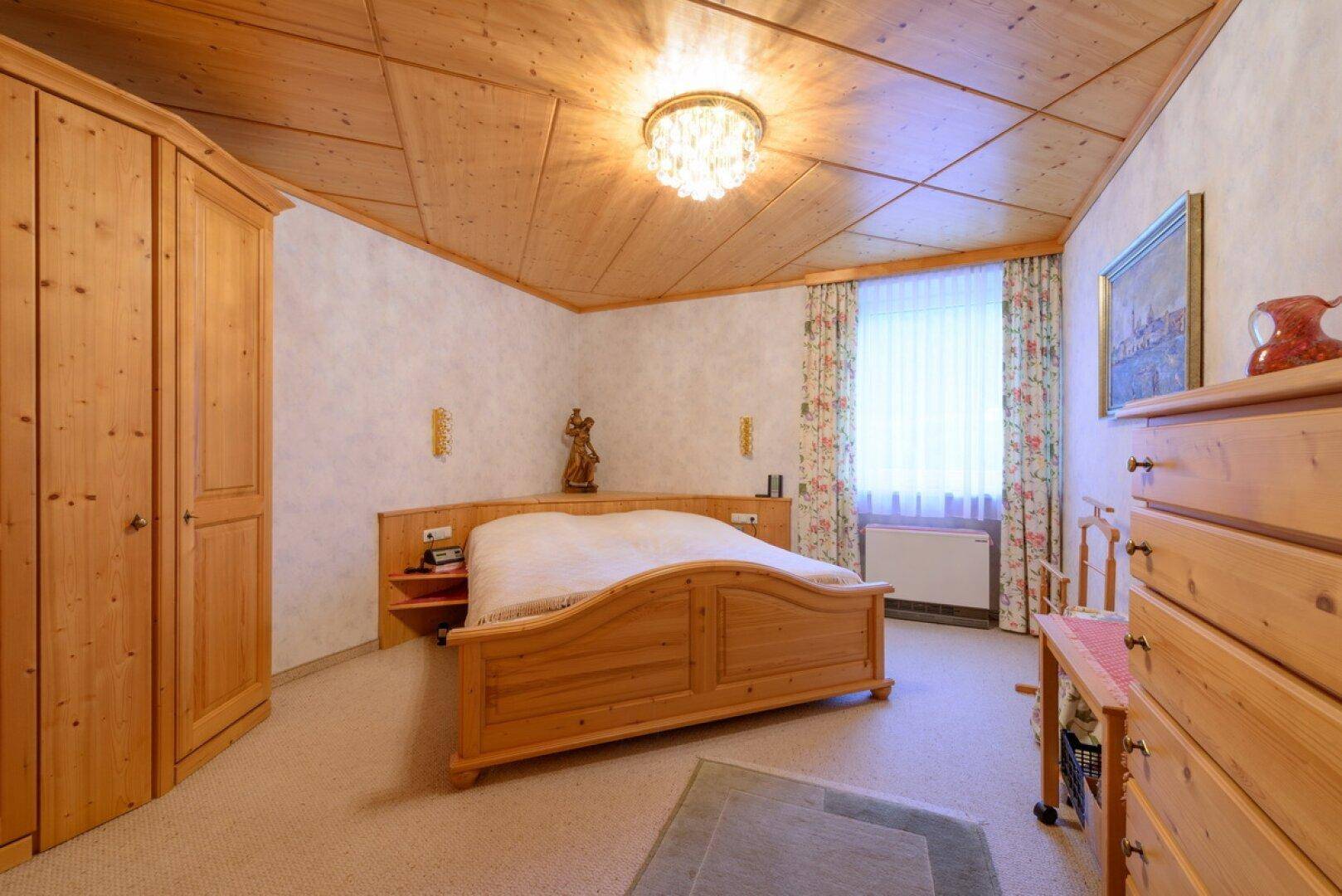 Gemütliches Schlafzimmer im Landhausstil mit Holzmöbeln, Teppichboden und Holzbalkendecke.