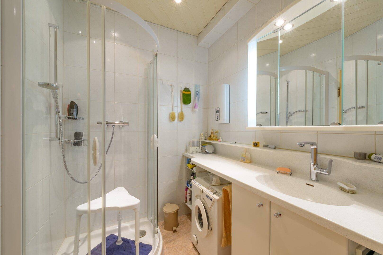 Helles Badezimmer mit Duschkabine, Waschbecken und integrierter Waschmaschine.