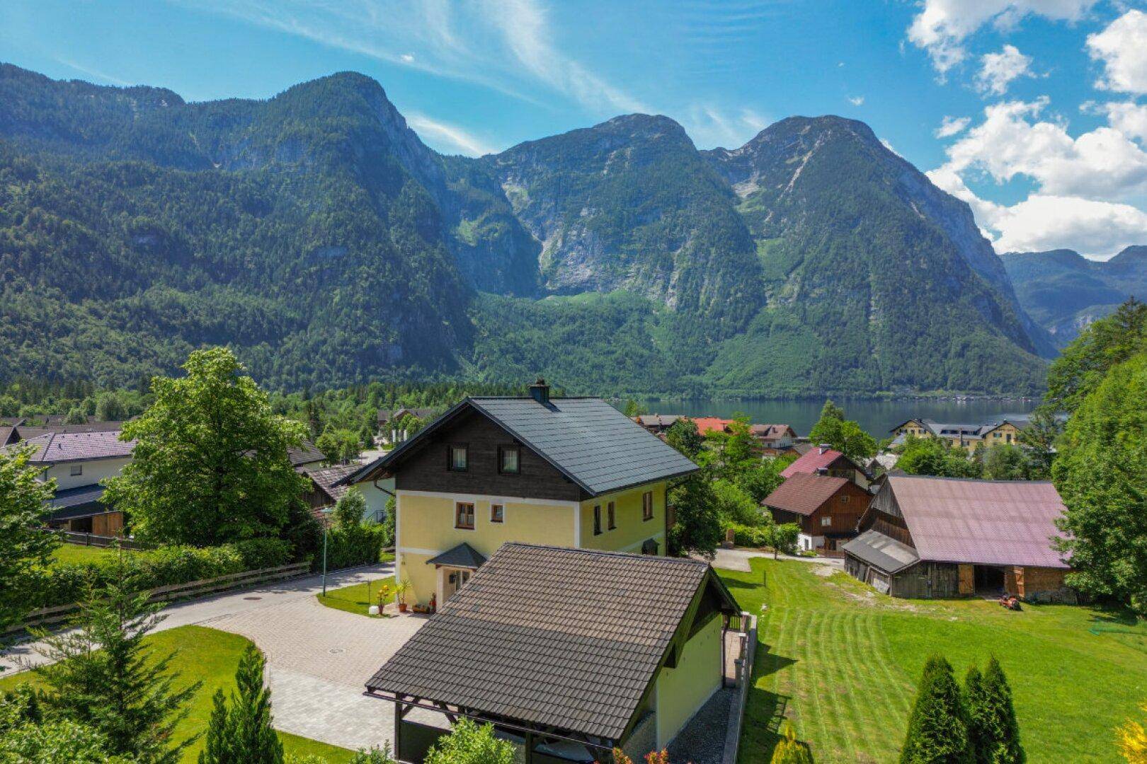 Luftaufnahme eines gelben Hauses mit Seeblick und Bergblick in einer ländlichen Umgebung.