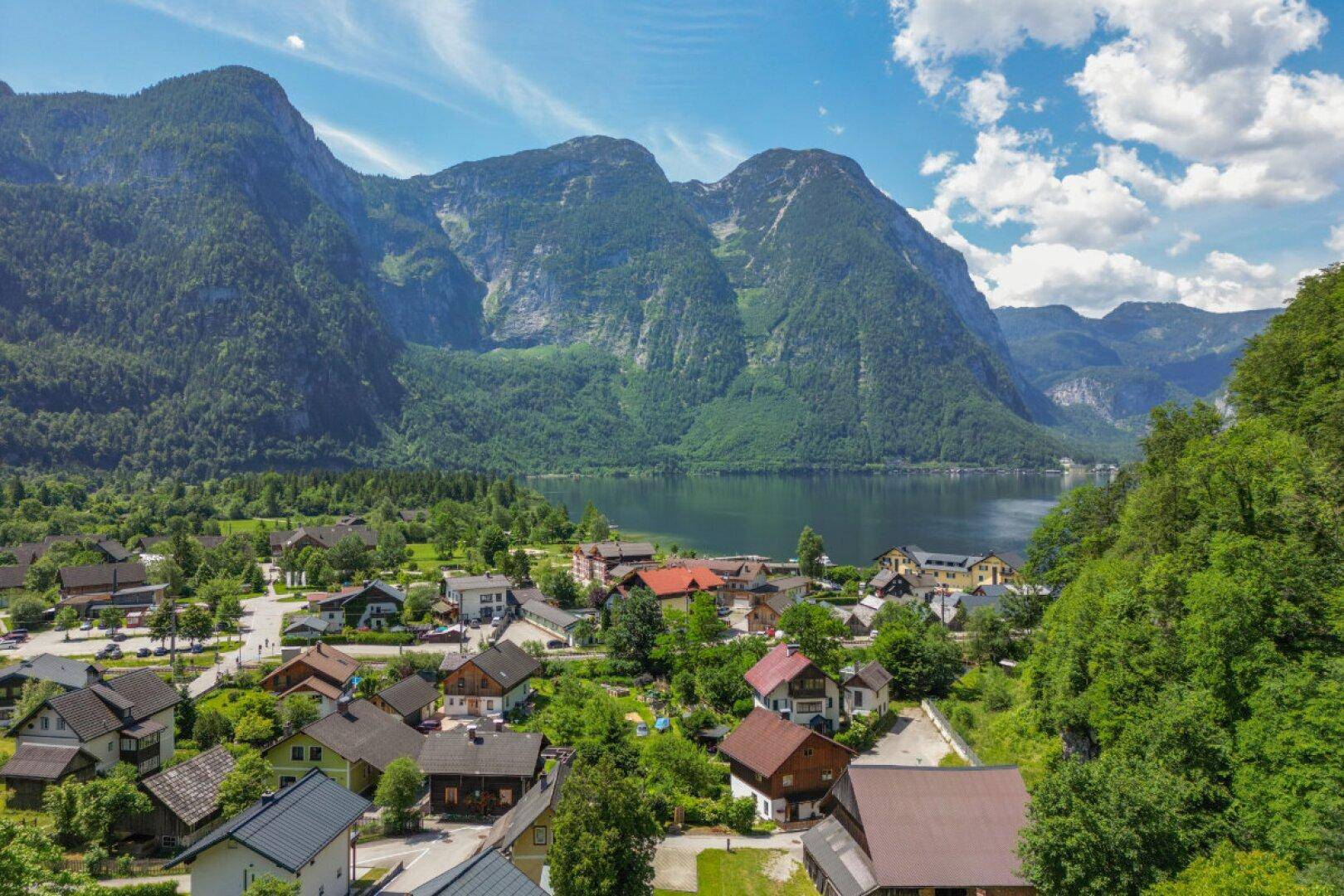 Panoramablick auf ein malerisches Dorf am Seeufer, umgeben von majestätischen Bergen und grüner Natur.