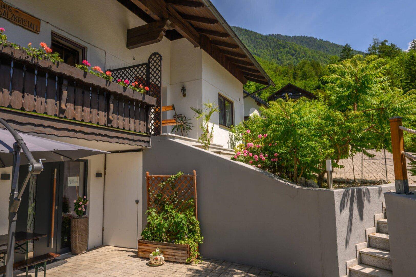 Gepflasterte Terrasse mit Sonnenschirm und Sitzgelegenheiten, umgeben von üppigem Grün und Stufen.