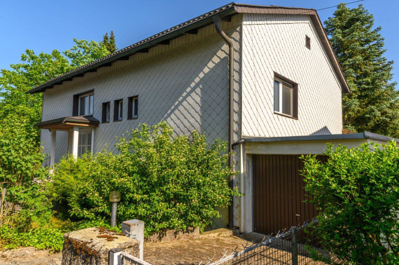 Seitenansicht des Wohnhauses mit integrierter Garage und gepflegter Bepflanzung.