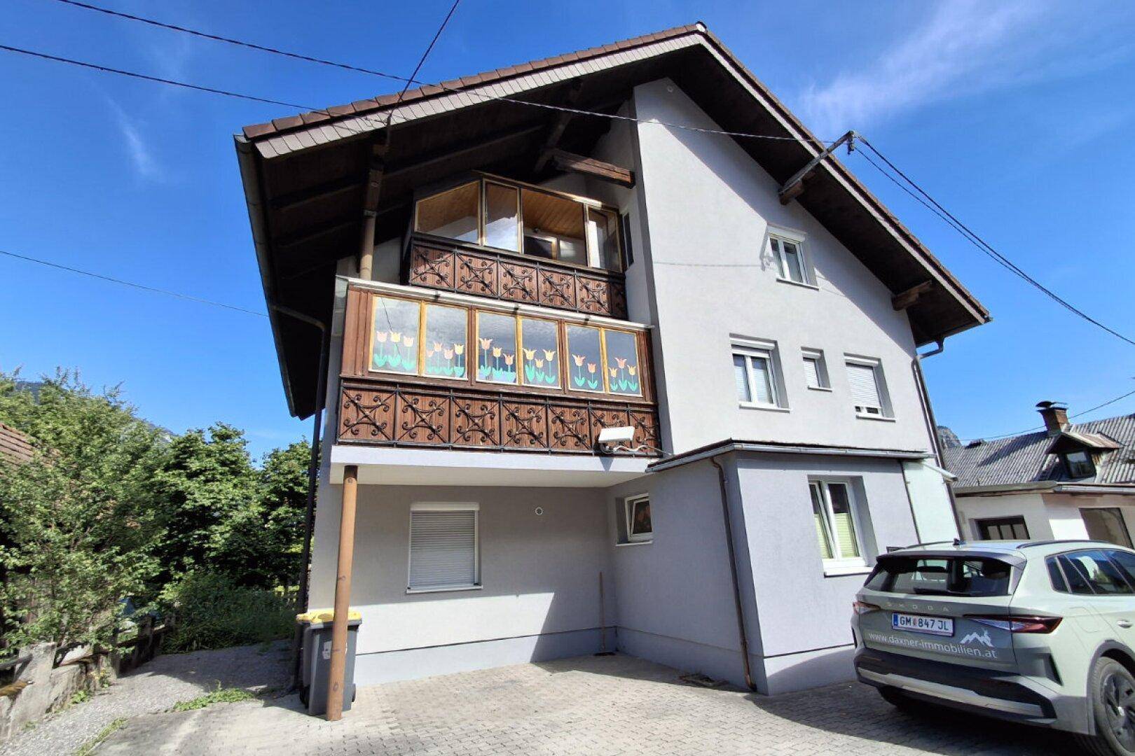 Außenansicht des Gebäudes mit Balkon und Stellplatz unter blauem Himmel.