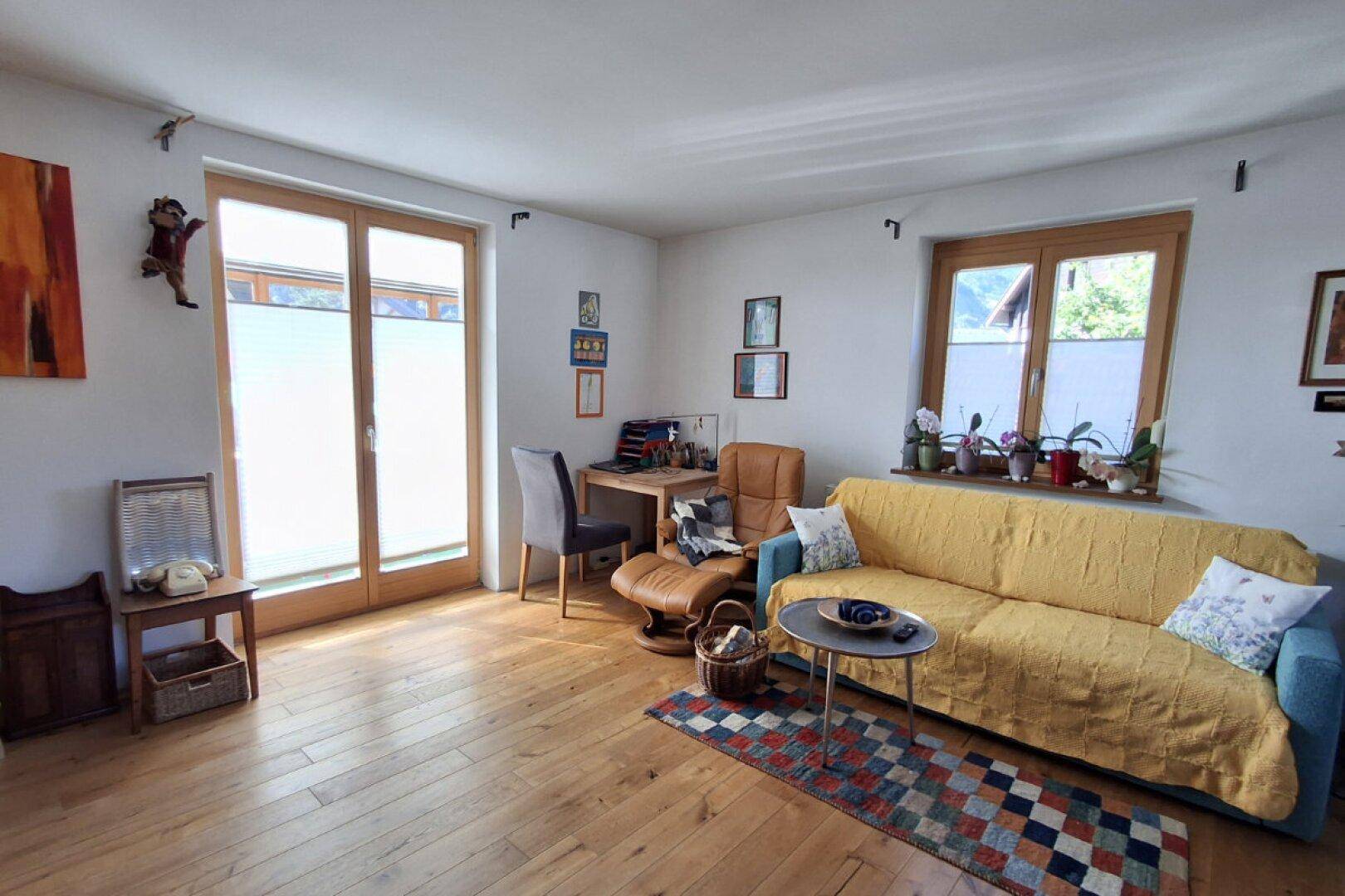 Helles Wohnzimmer mit Holzboden, Sofa und Zugang zu einem Balkon.