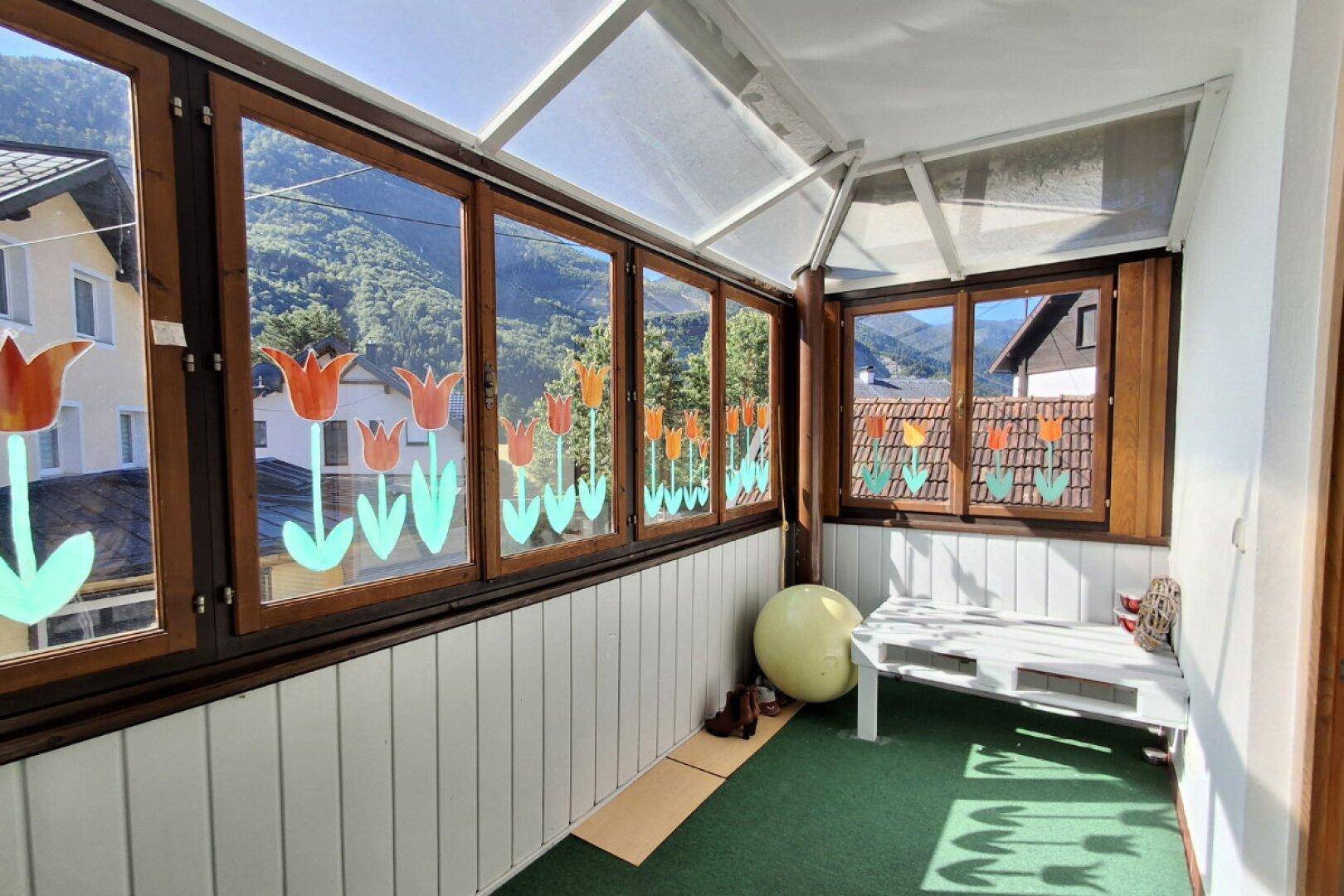 Verglaste Loggia mit Blick auf die Berge und grüne Umgebung.