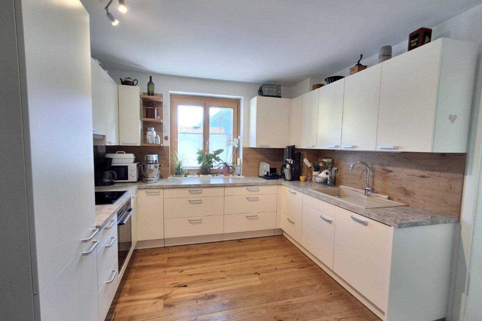 Moderne Einbauküche mit weißen Schränken, Holzrückwand und Fenster.