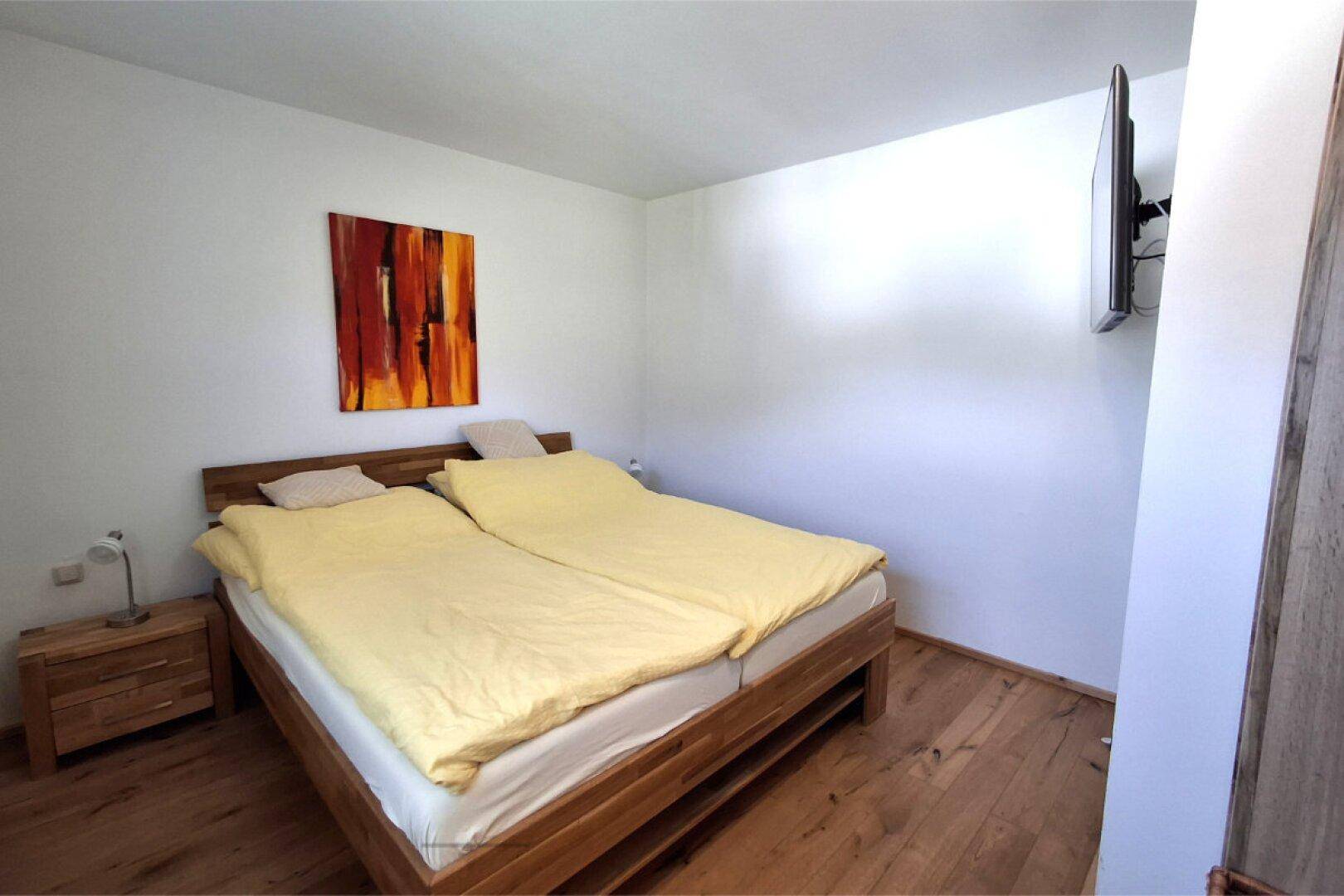 Schlafzimmer mit Holzbett, Nachttisch und Holzboden.