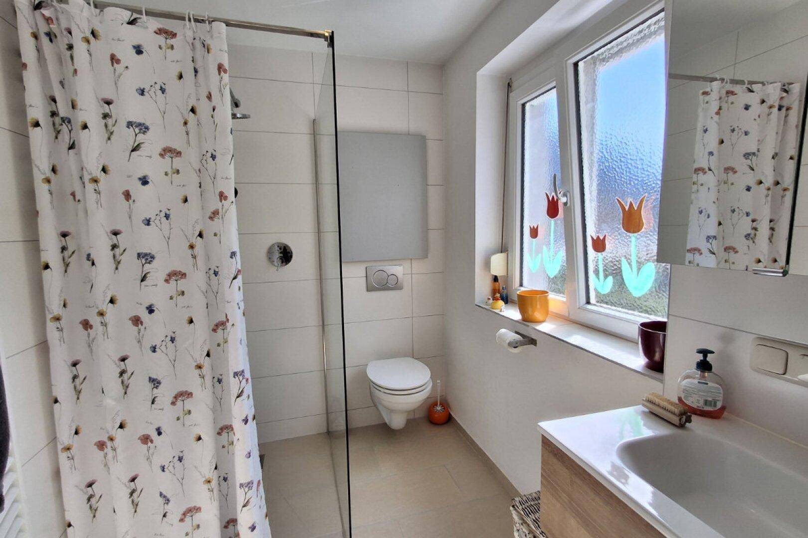 Modernes Badezimmer mit Dusche, WC, Waschbecken und Fenster.