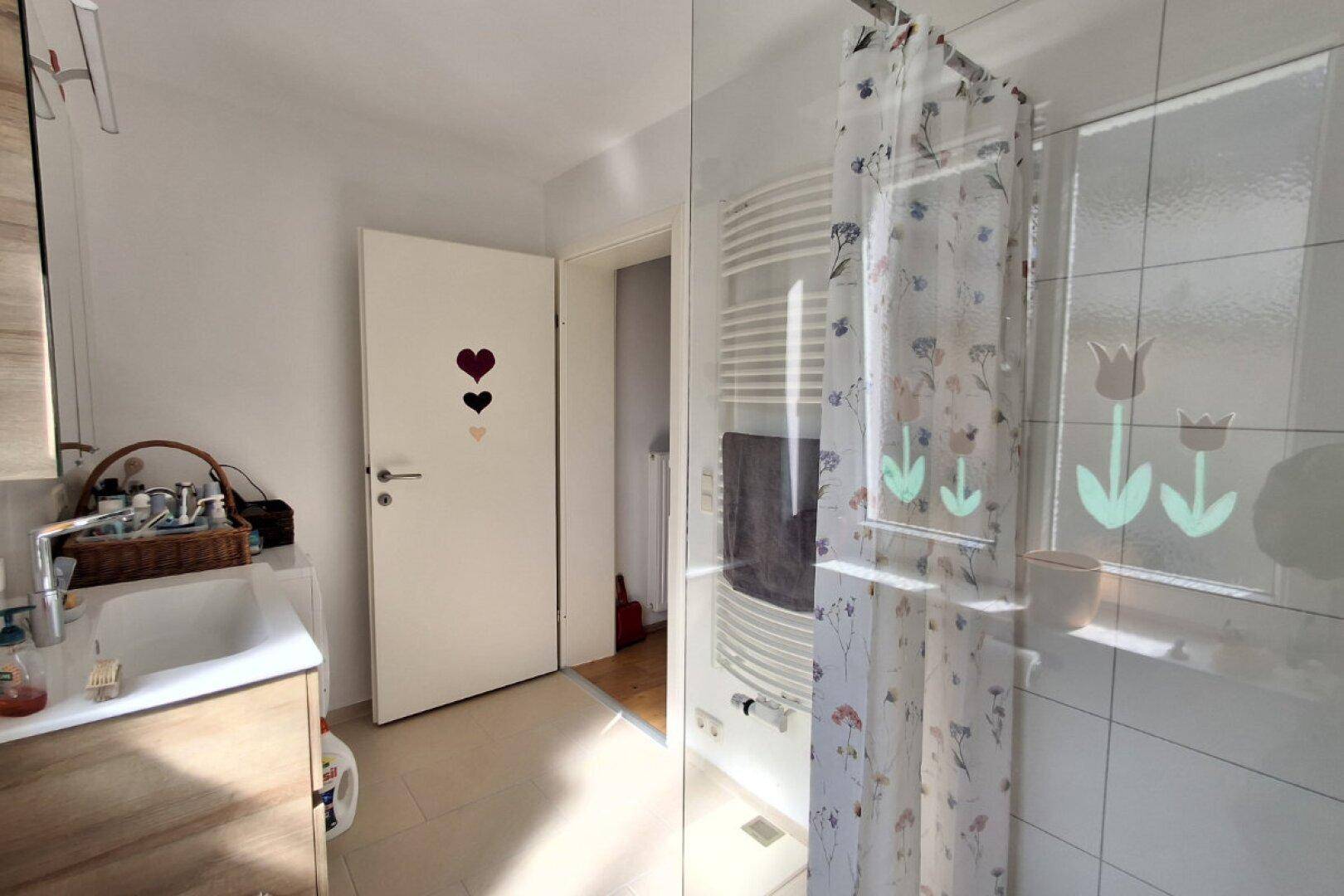 Helles Badezimmer mit Dusche, beheiztem Handtuchhalter und Fenster.