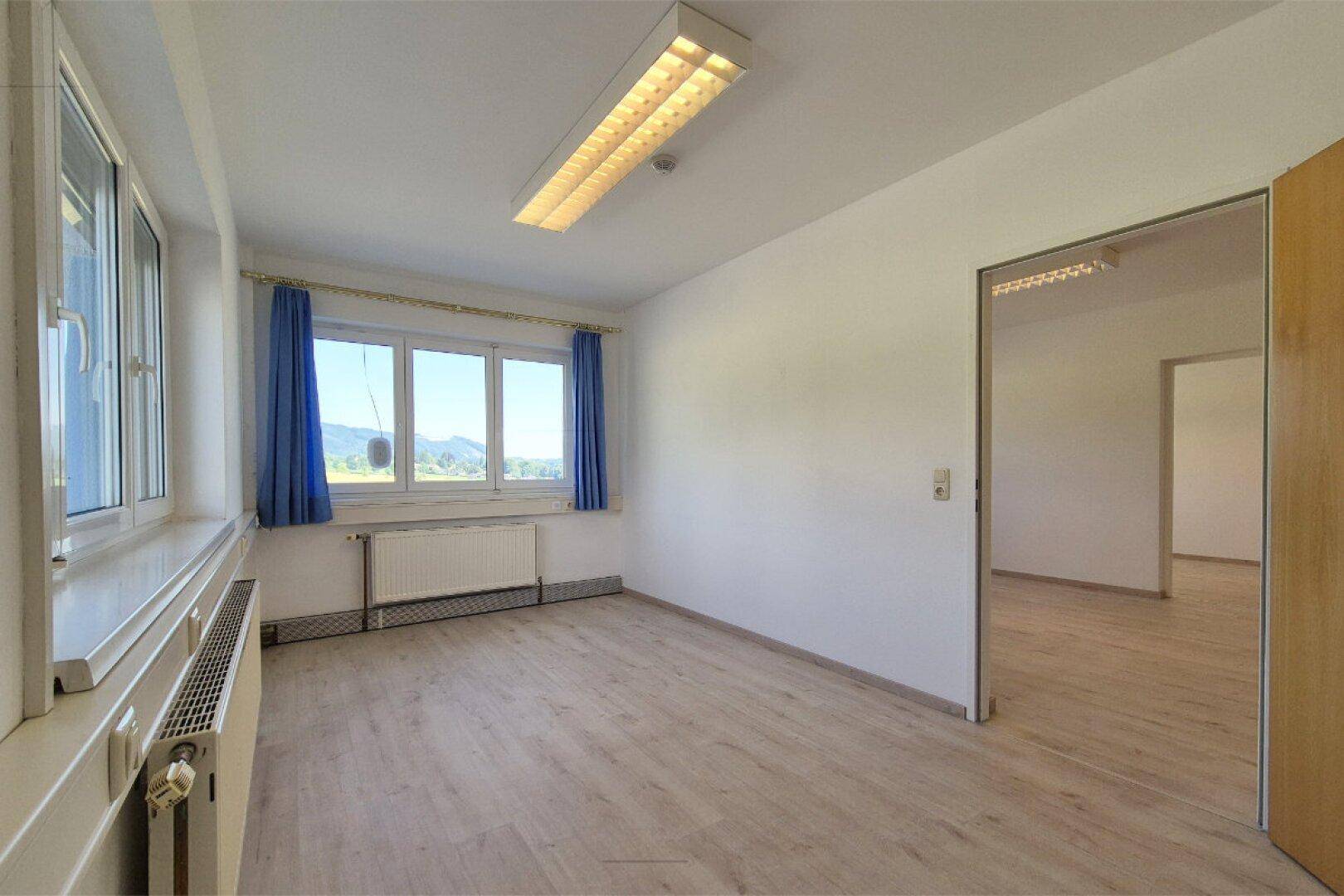 Geräumiges Bürozimmer mit Laminatboden, großen Fenstern und einem schönen Ausblick auf die Natur.