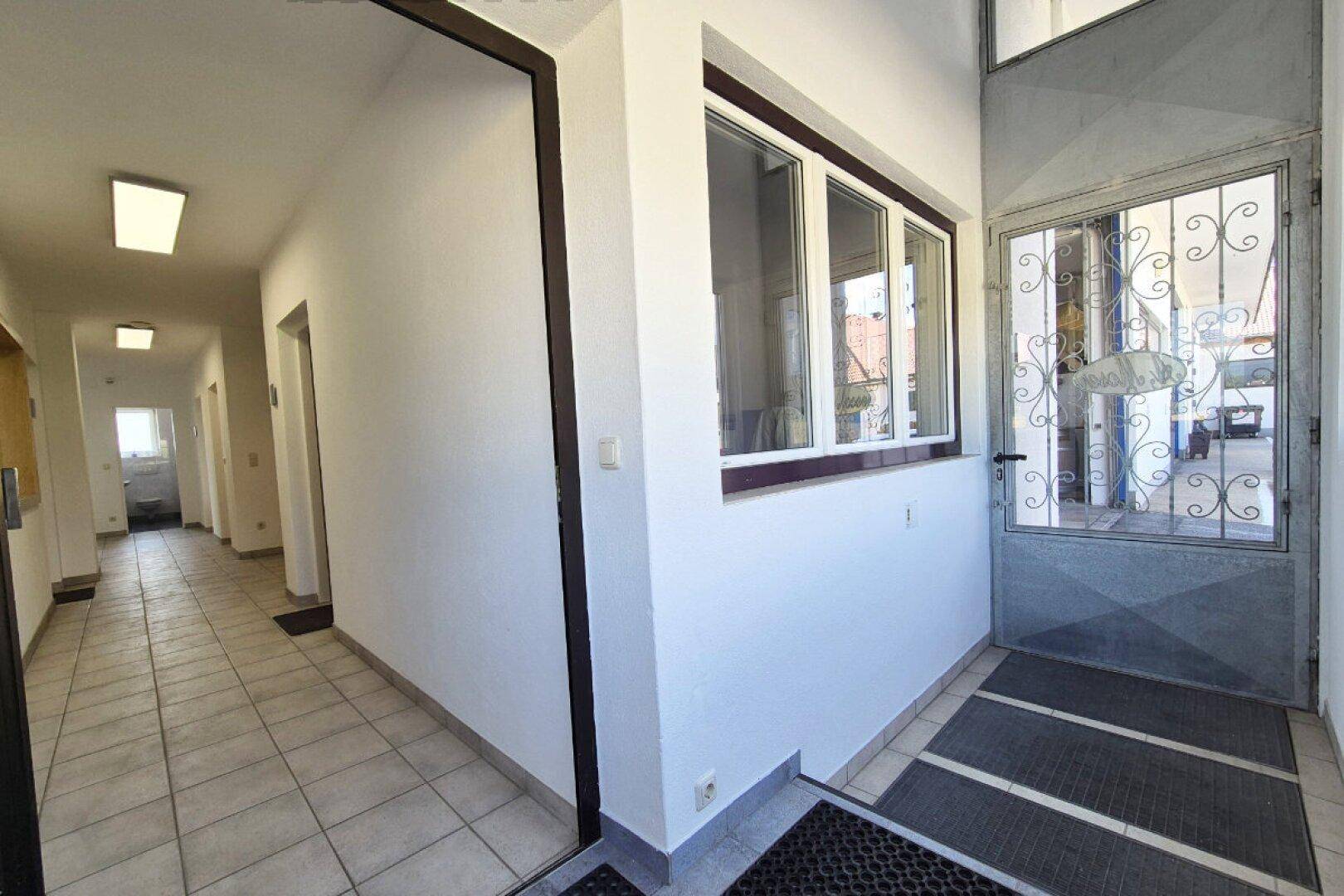 Heller Eingangsbereich mit Fliesenboden und einer Glastür, die ins Freie führt.