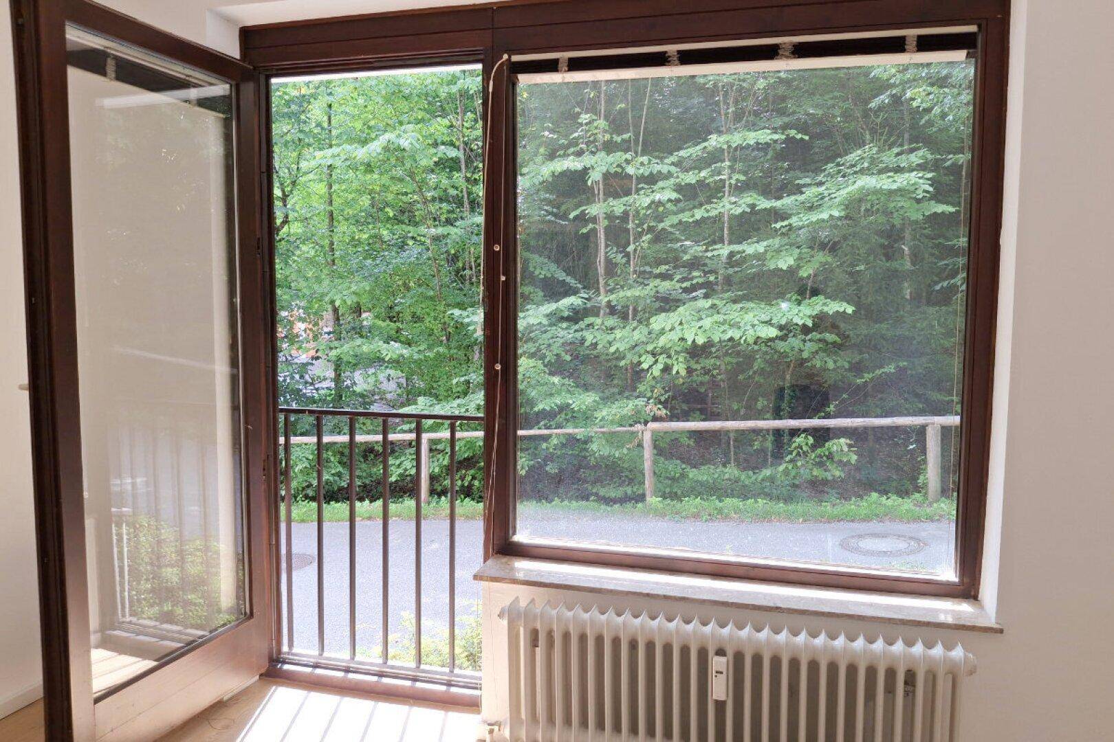 Heller Raum mit Zugang zu einem französischen Balkon und Blick auf Bäume und einen Weg.