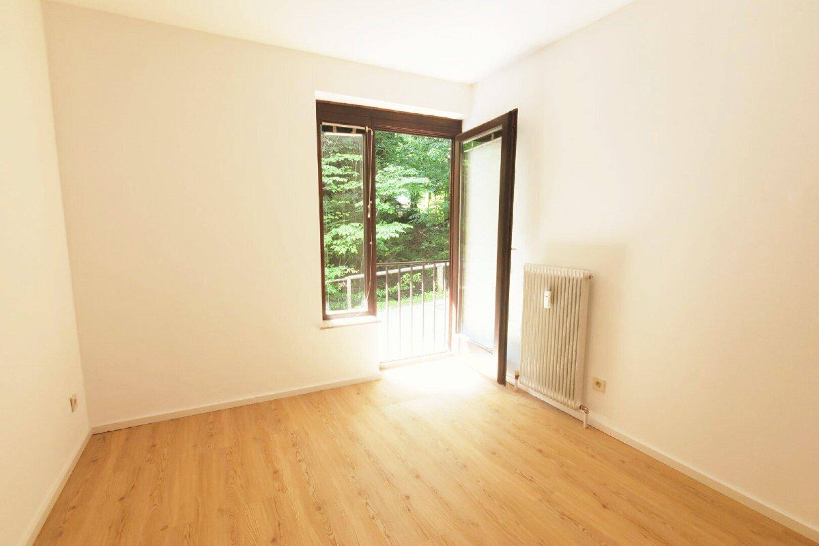 Heller Wohnraum mit Holzboden, Zugang zu einem französischen Balkon und Blick ins Grüne.