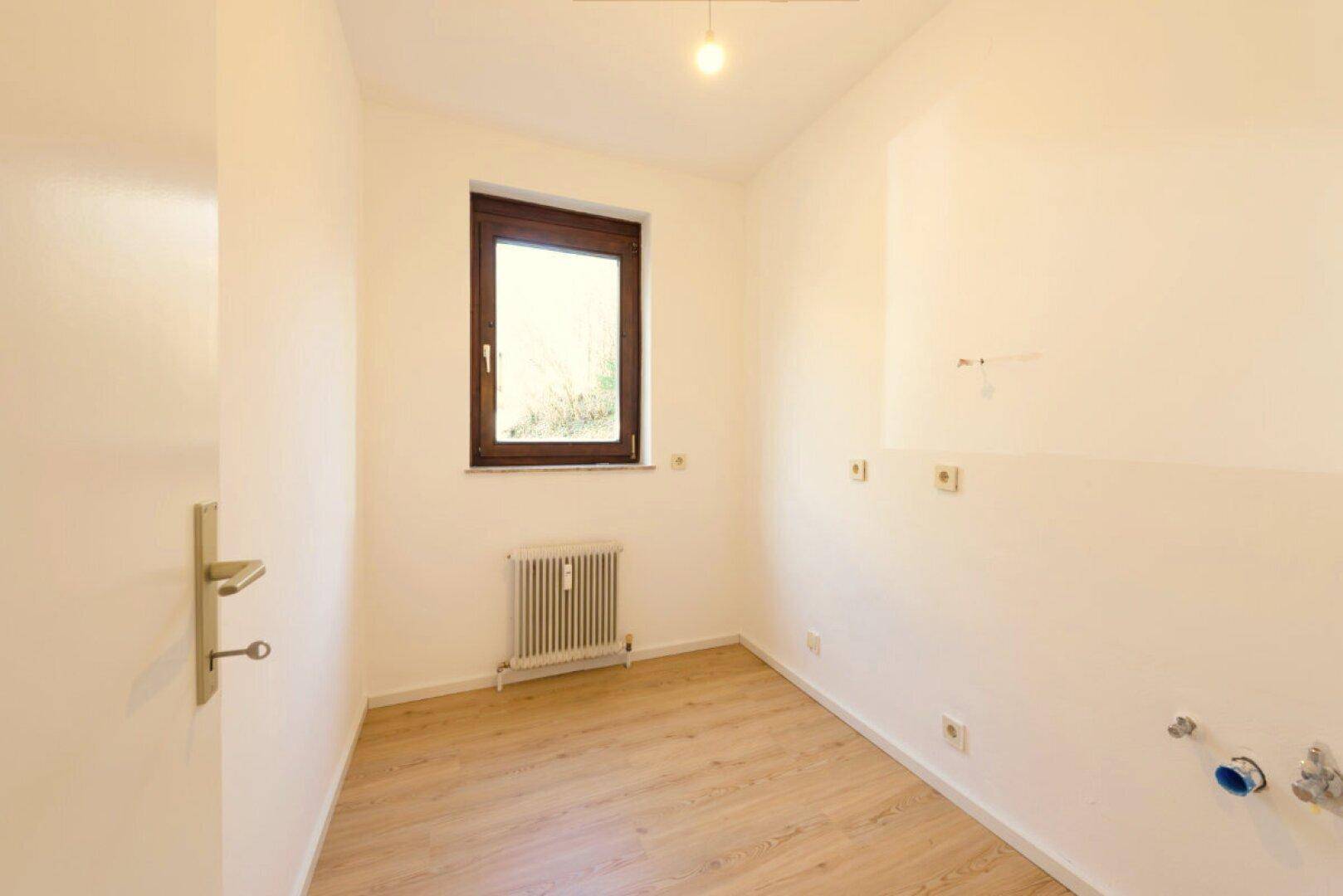 Kleiner leerer Raum mit Fenster, Heizkörper und Anschlüssen für eine mögliche Nutzung.