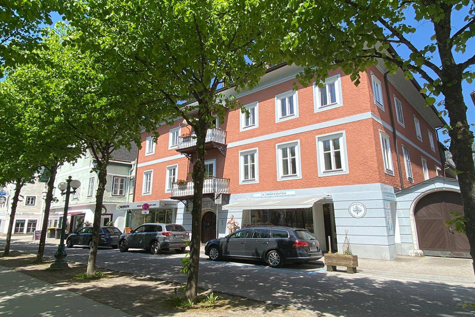 Ansicht eines mehrstöckigen Gebäudes mit Geschäften im Erdgeschoss an einer belebten Straße.