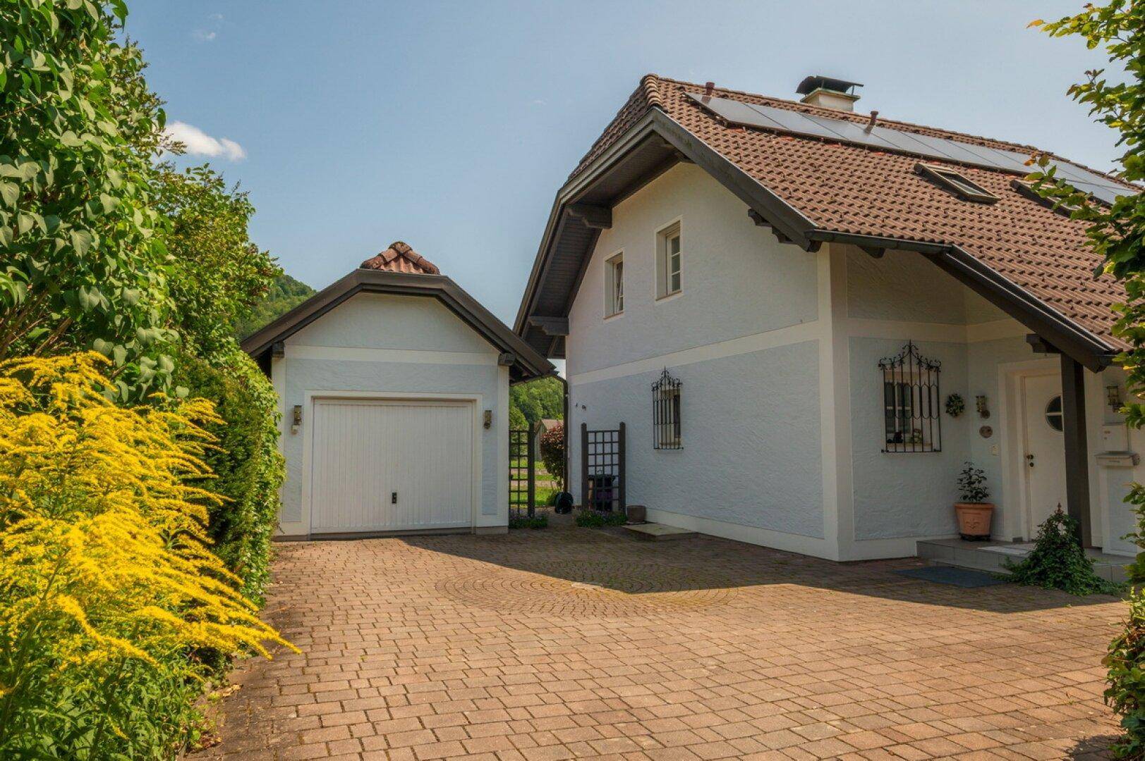 Ansicht des Hauses mit separater Garage und gepflasterter Auffahrt an einem sonnigen Tag.