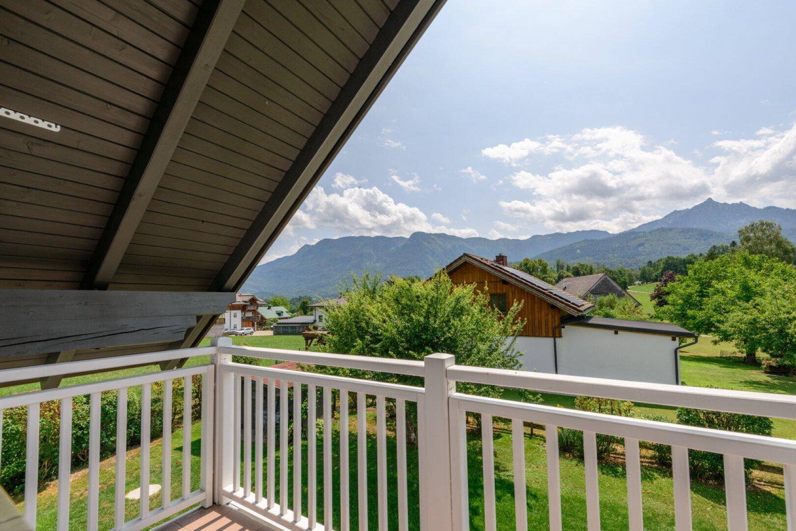 Balkon mit weißem Geländer und weitem Blick auf die umliegende Berglandschaft und grüne Wiesen.