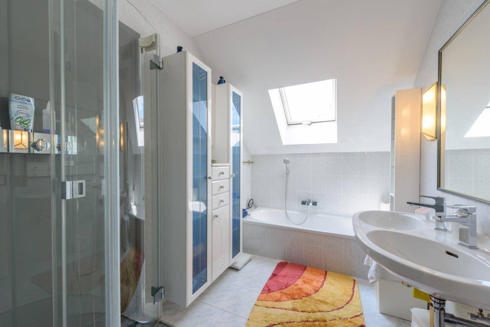 Helles Badezimmer mit Dusche, Badewanne unter einem Dachfenster und modernem Waschtisch.
