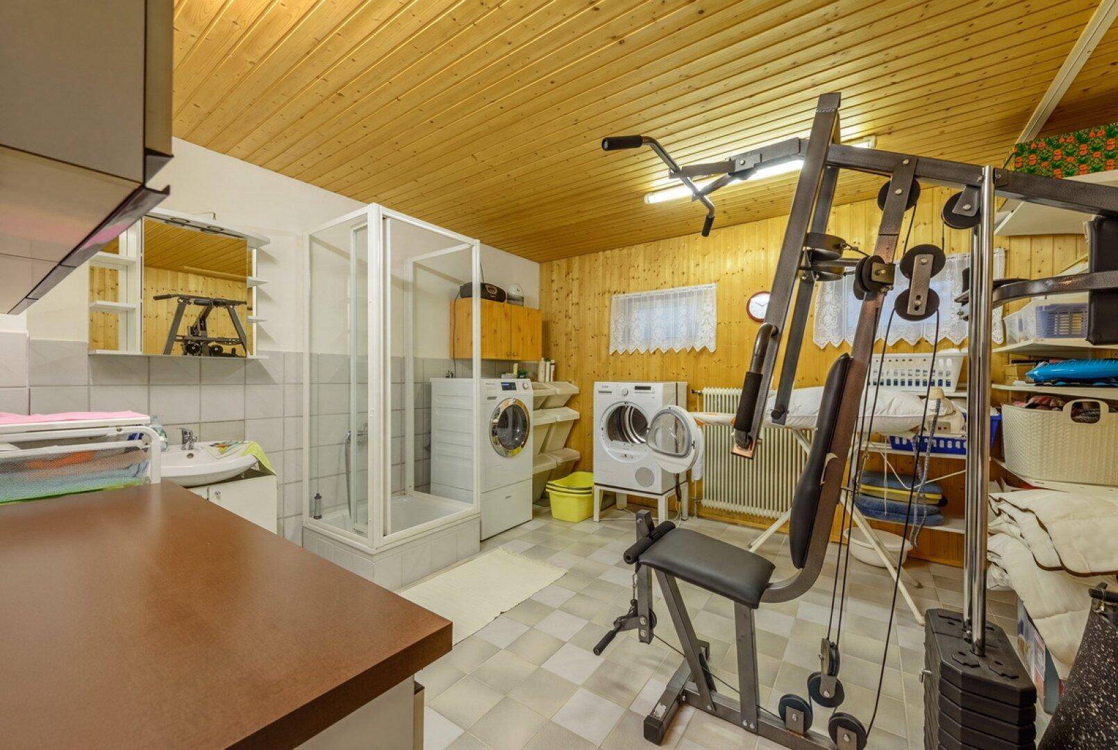 Funktionaler Hauswirtschaftsraum mit Waschmaschine, Trockner, Dusche und Fitnessgeräten.