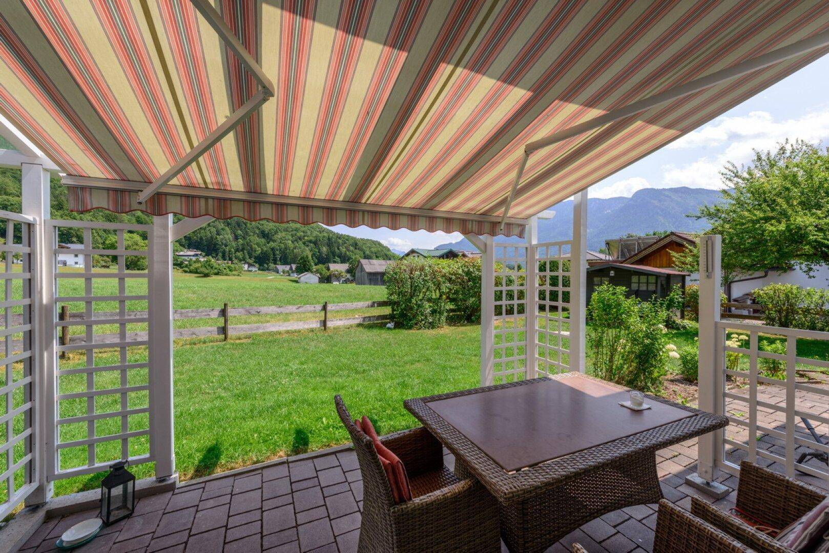 Überdachte Terrasse mit Sitzgelegenheiten, Blick auf grüne Wiesen und die umliegenden Berge.