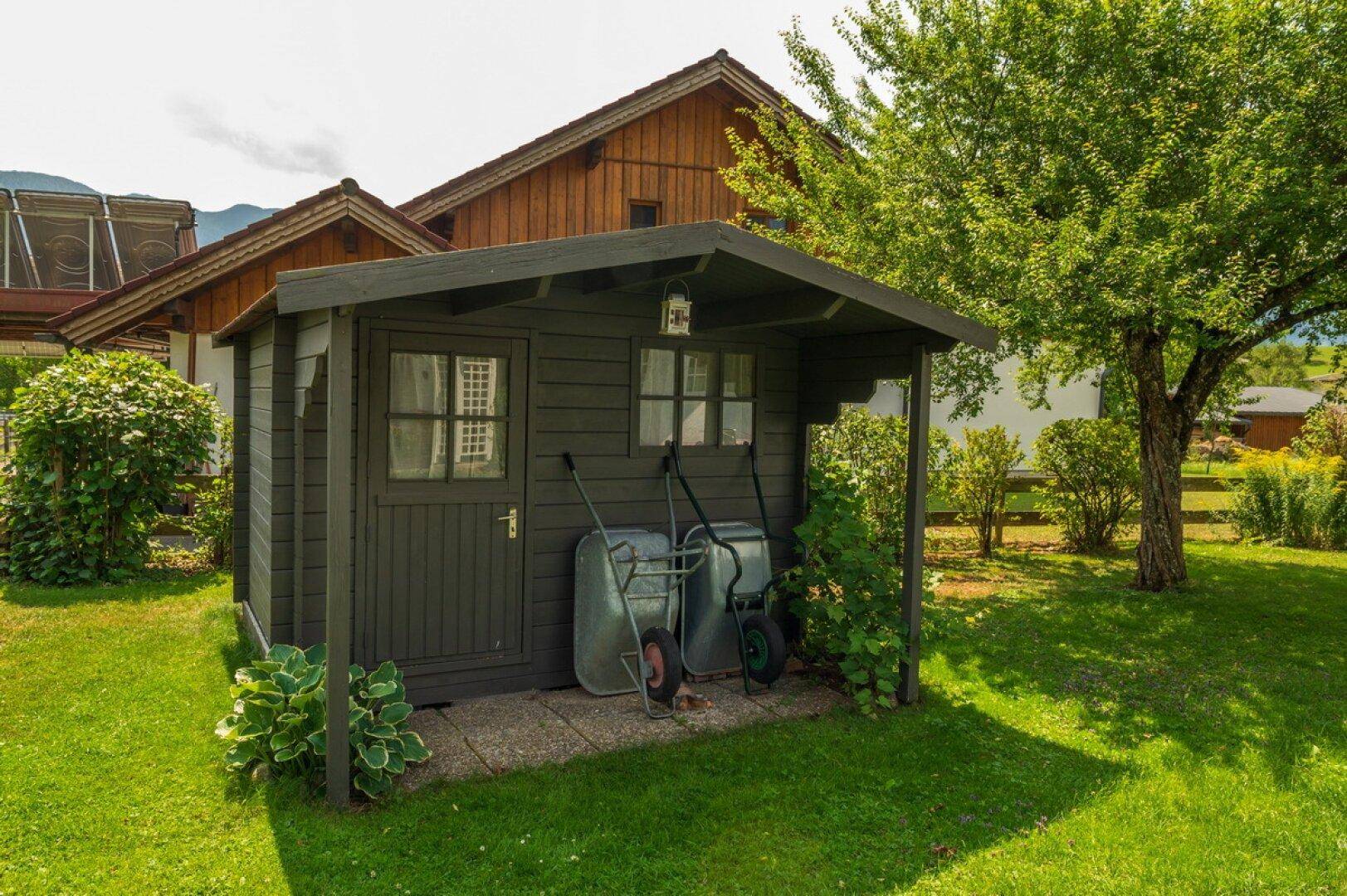 Gepflegter Garten mit Gartenhaus und Rasenfläche, umgeben von Bäumen und Sträuchern.
