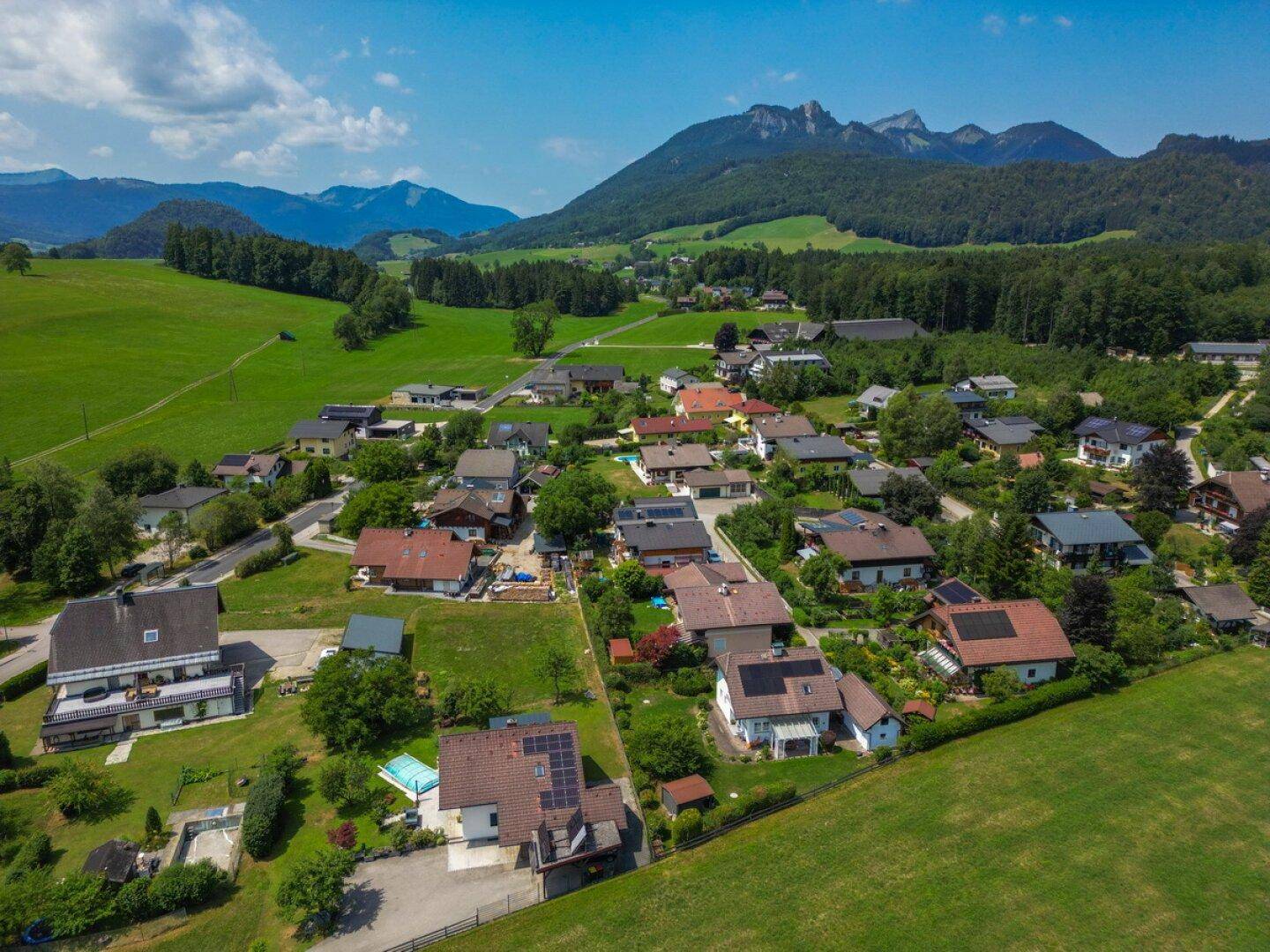 Weitläufige Luftaufnahme der Wohnsiedlung mit grünen Feldern und majestätischen Bergen.