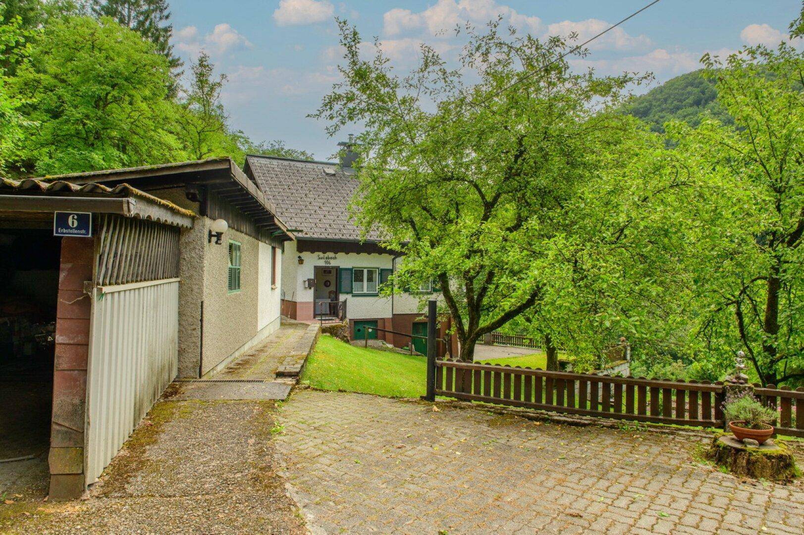 Einfahrt zum Haus mit angrenzender Garage und viel Grün in ländlicher Umgebung.