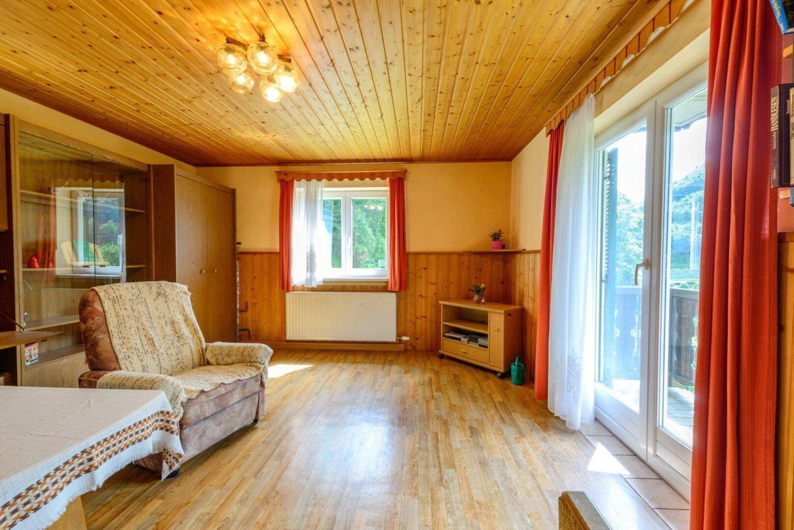 Gemütliches Wohnzimmer mit Holzvertäfelung, Holzbalkendecke und Zugang zum Balkon.