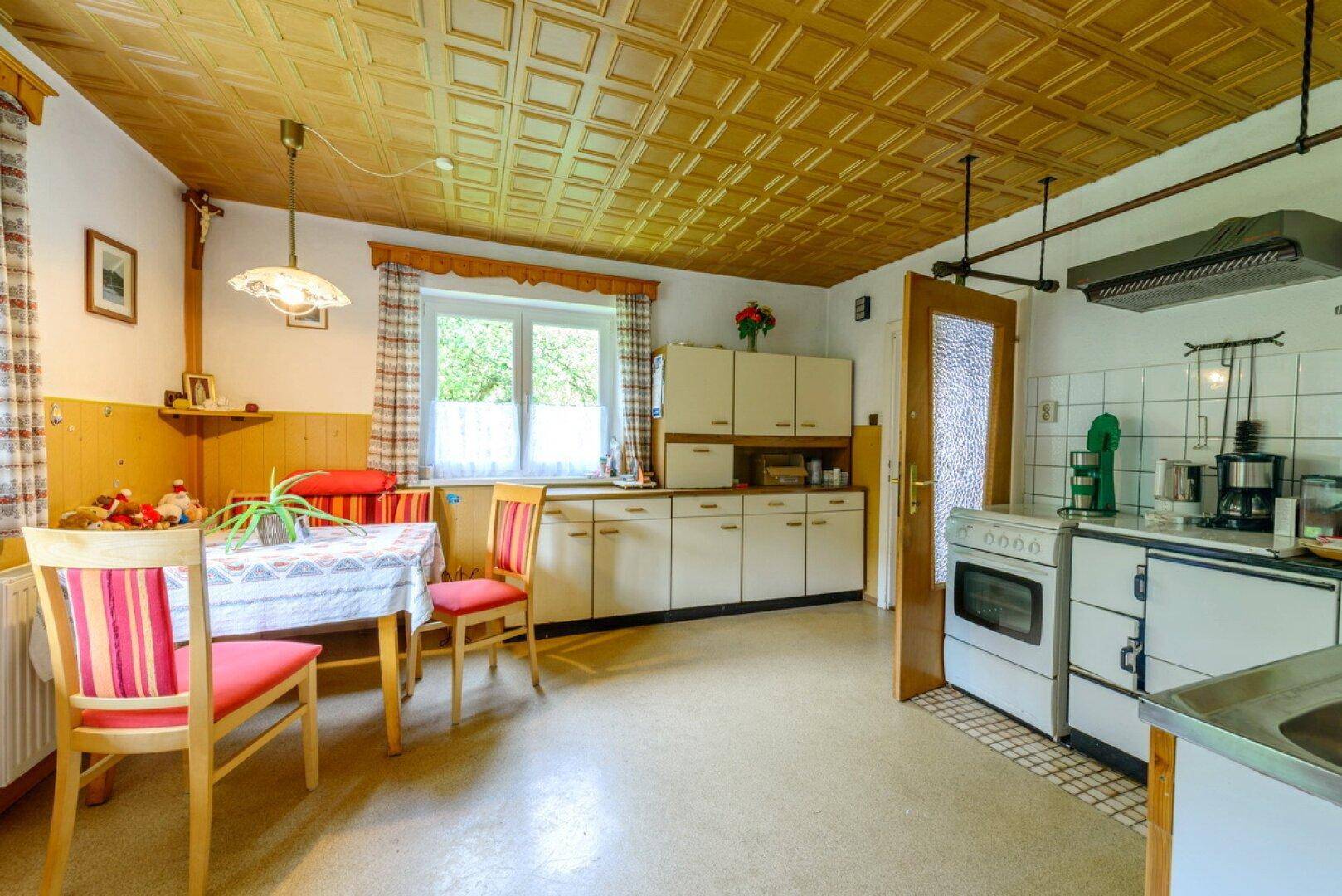 Traditionelle Küche mit Essbereich, älteren Einbauschränken und gemusterter Decke.
