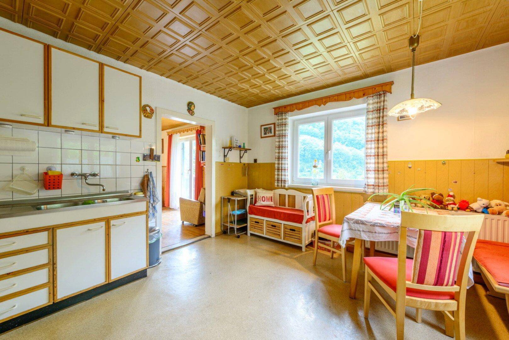 Helle Küche mit Essplatz, Holzvertäfelung und Blick ins Grüne durch das Fenster.