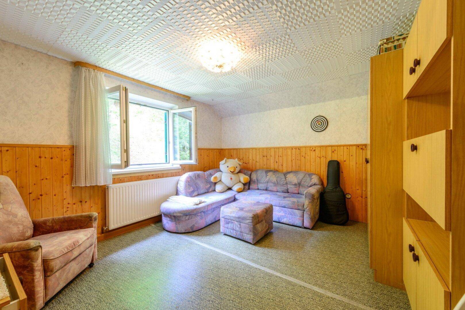 Gemütlicher Wohnbereich mit Sofa, Sessel und Holzvertäfelung, ideal zum Entspannen.