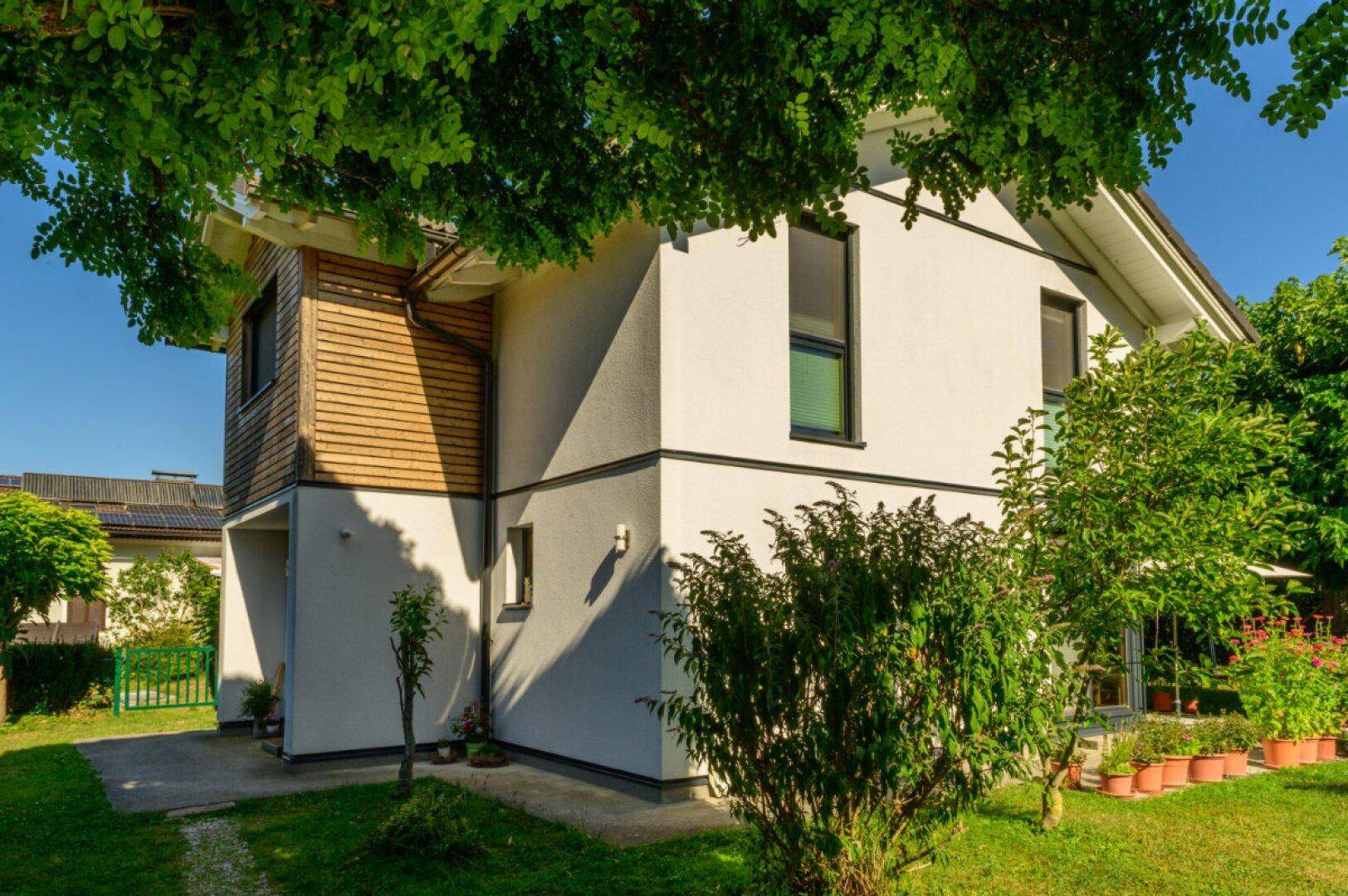 Modernes Einfamilienhaus mit Holzverkleidung und weißer Fassade, umgeben von grüner Natur.