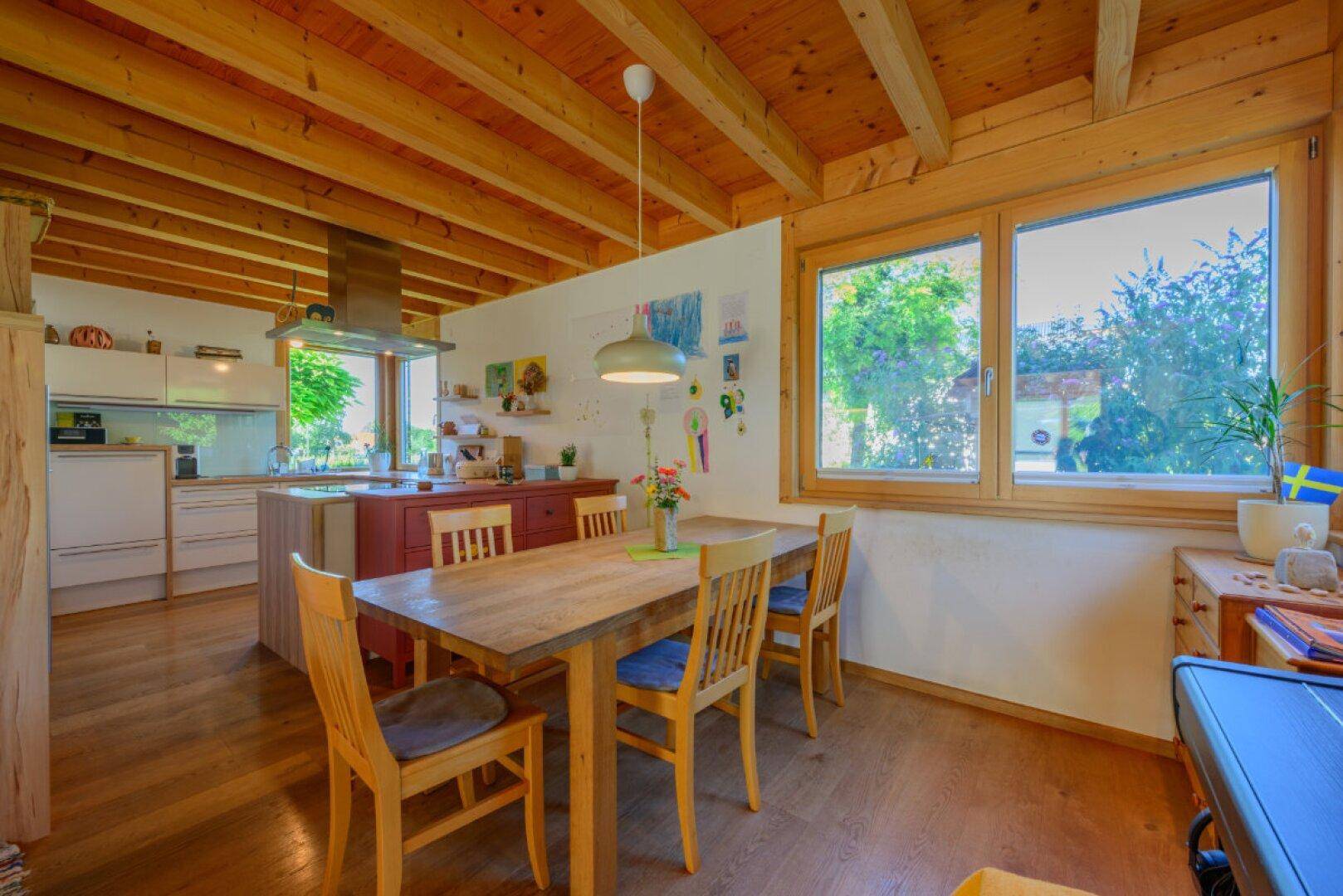 Offener Essbereich mit Holztisch und Stühlen, angrenzend an eine moderne Küche mit Holzbalkendecke.