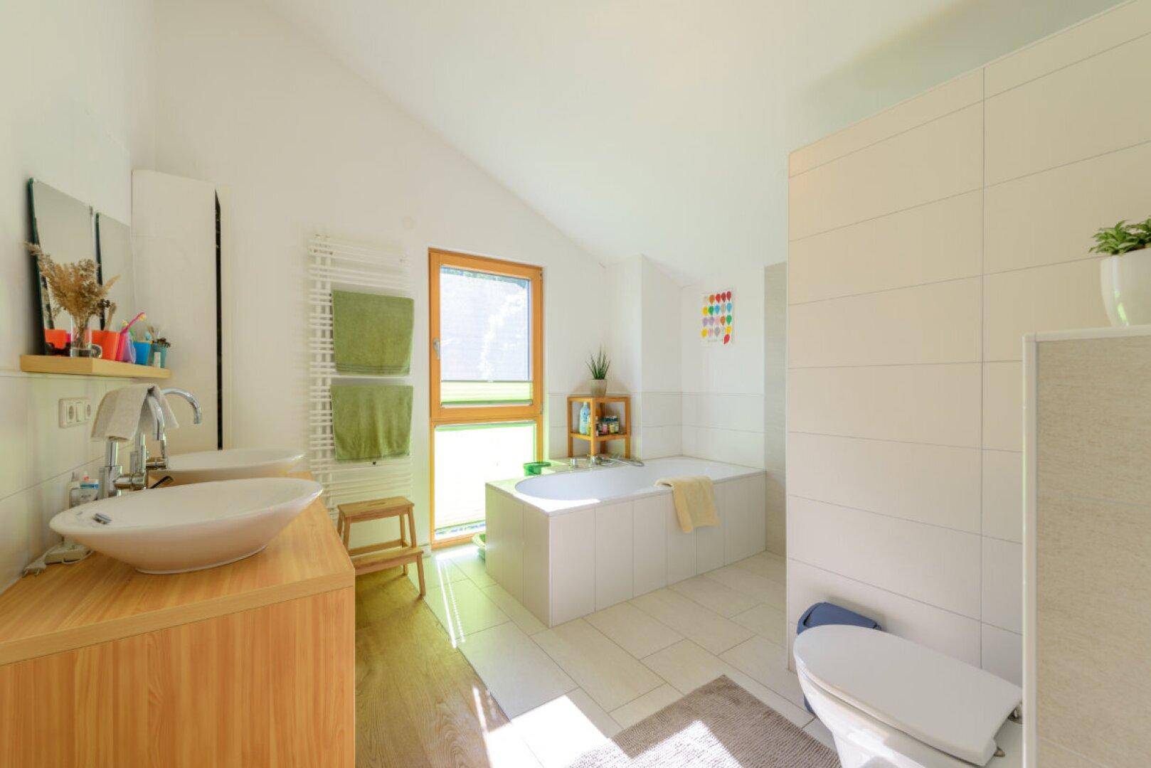 Helles Badezimmer mit Badewanne, modernem Waschbecken, WC und Fenster unter einer Dachschräge.