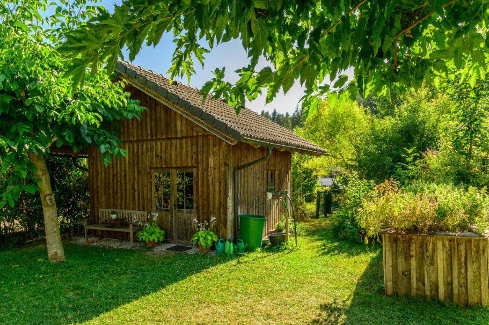 Rustikales Gartenhaus aus Holz mit Sitzbank und Hochbeet in einem grünen Garten.