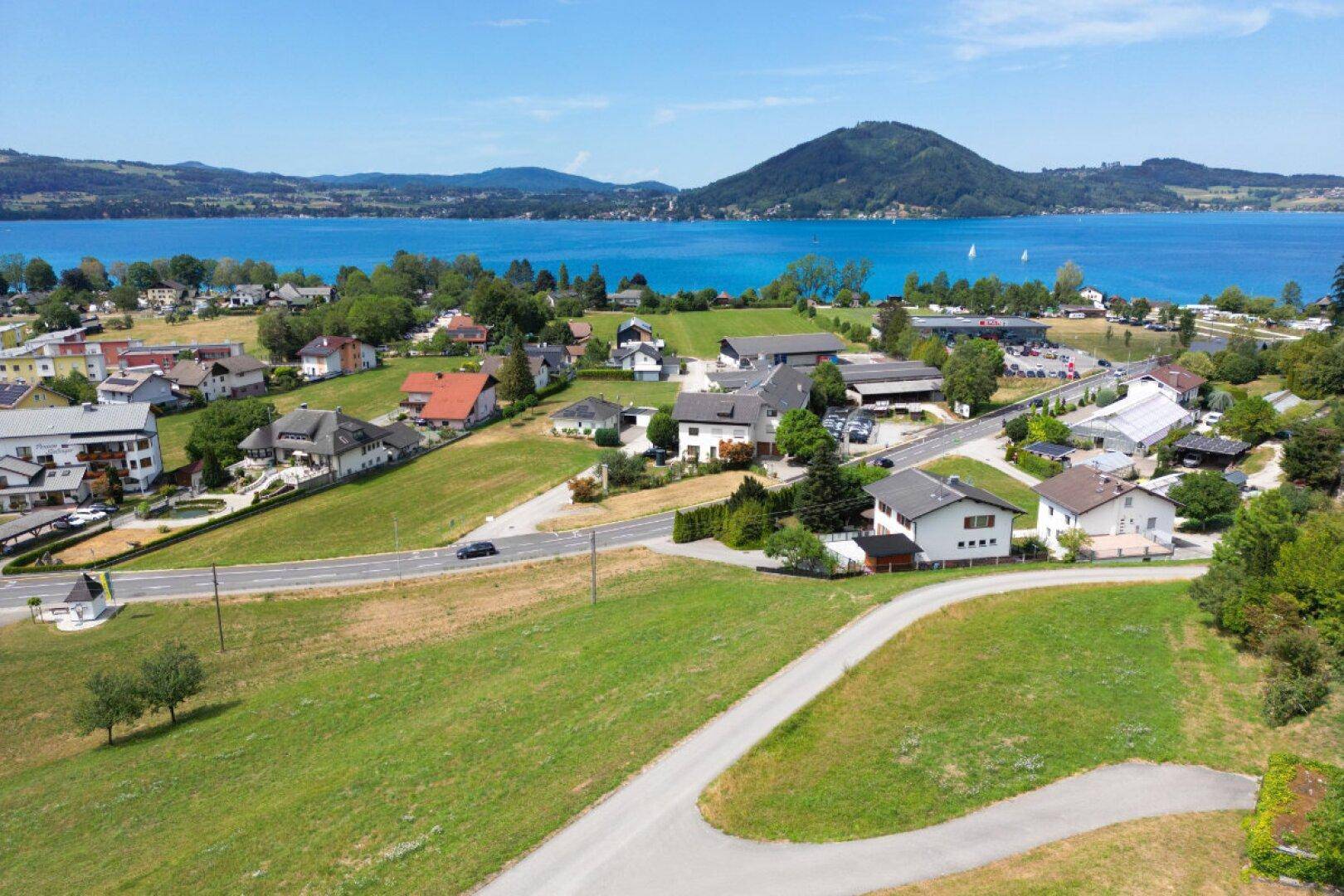 Weitläufige Luftaufnahme einer Siedlung am Attersee mit umliegenden Feldern und Bergen.