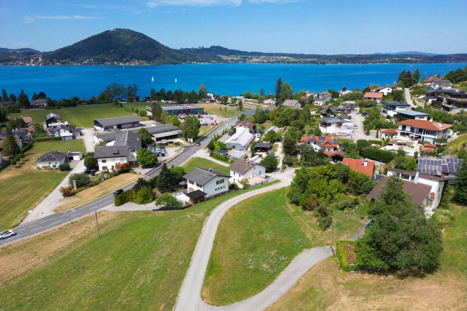 Luftaufnahme einer Wohnsiedlung am Attersee mit grünen Hügeln und klarem blauen Wasser.