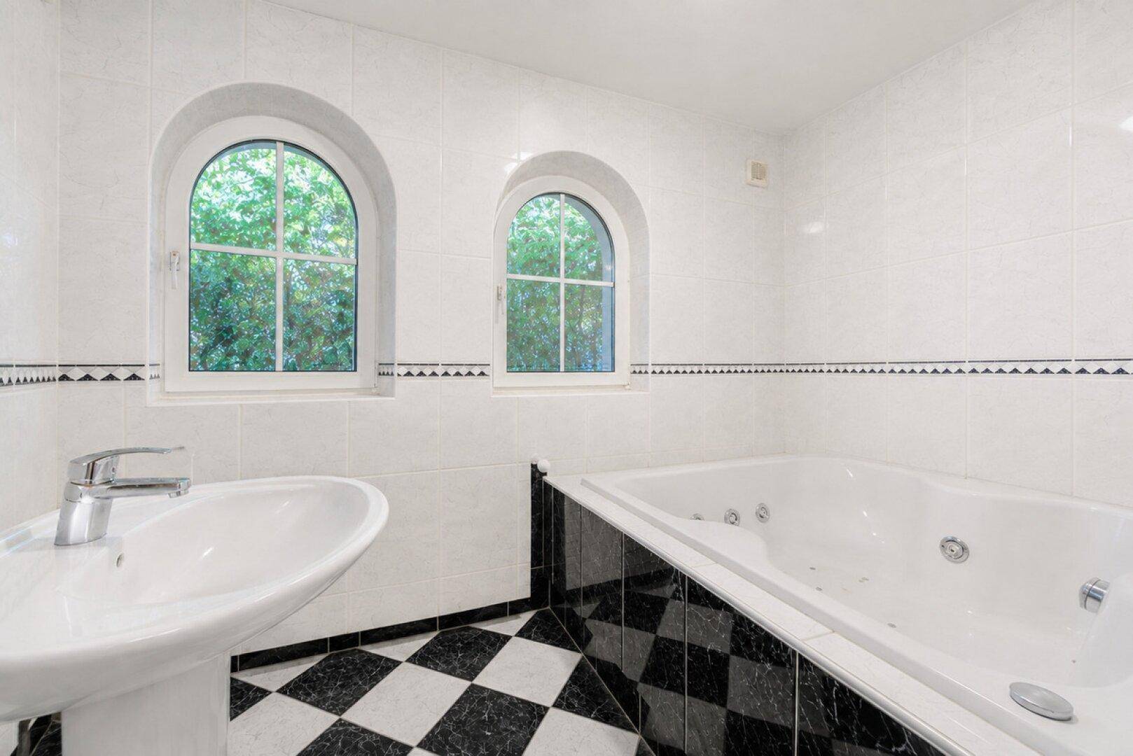 Badezimmer mit schwarz-weißem Fliesenboden, weiß gefliesten Wänden und Eck-Whirlpool.