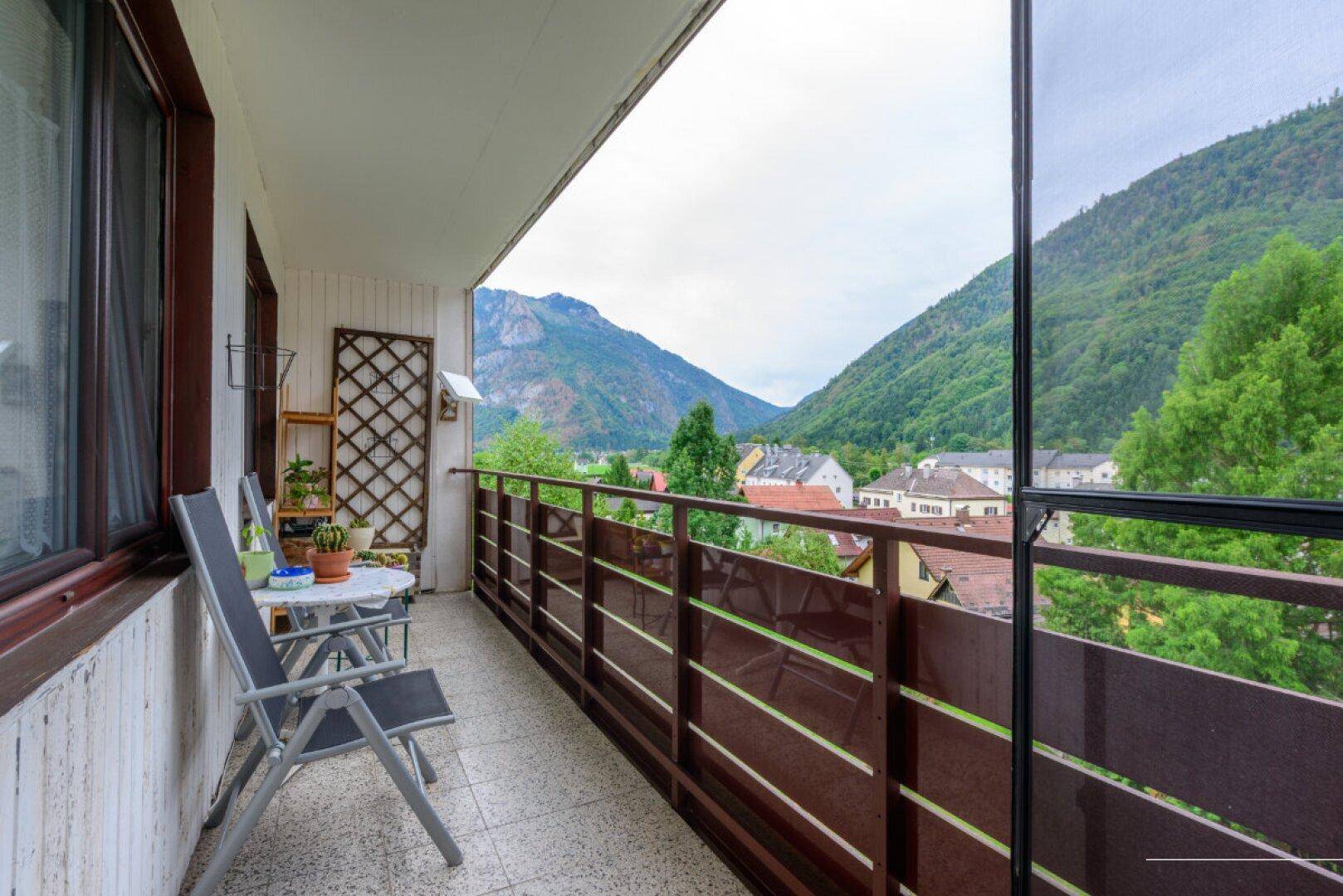 Balkon mit Sitzgelegenheiten und weitem Blick auf die umliegenden Berge und die Ortschaft.