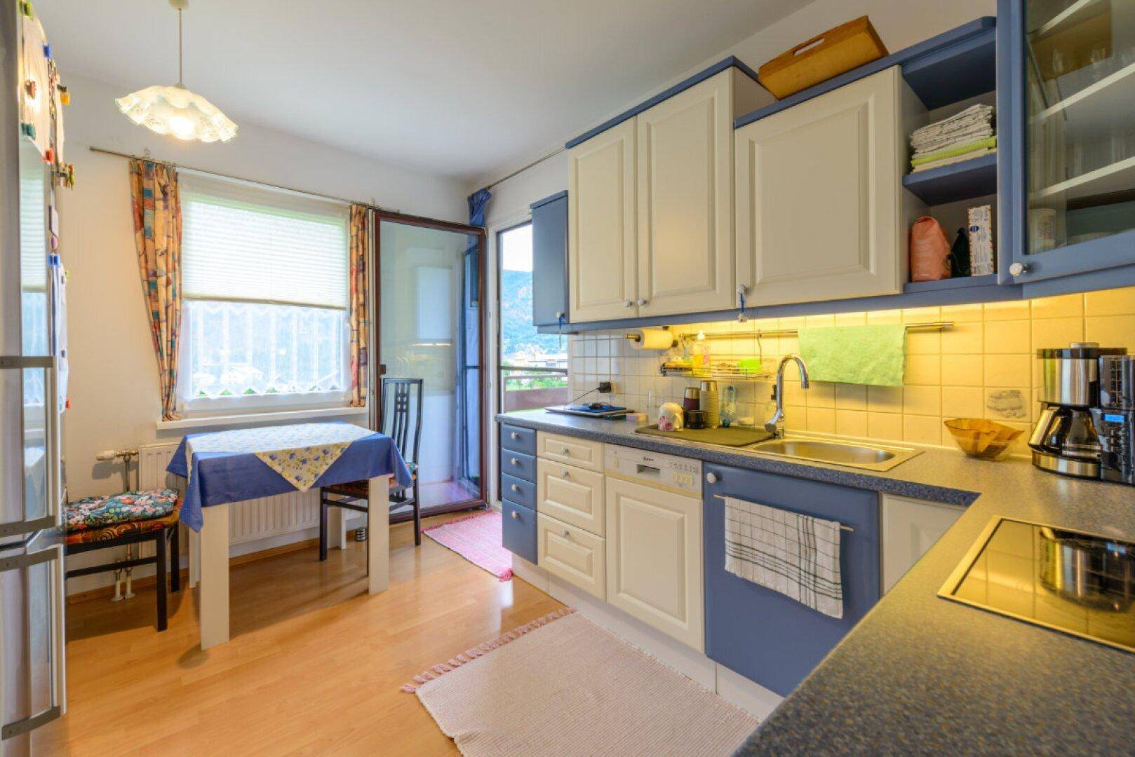 Funktionale Küche mit blauen und weißen Schränken, Essbereich und Zugang zum Balkon.